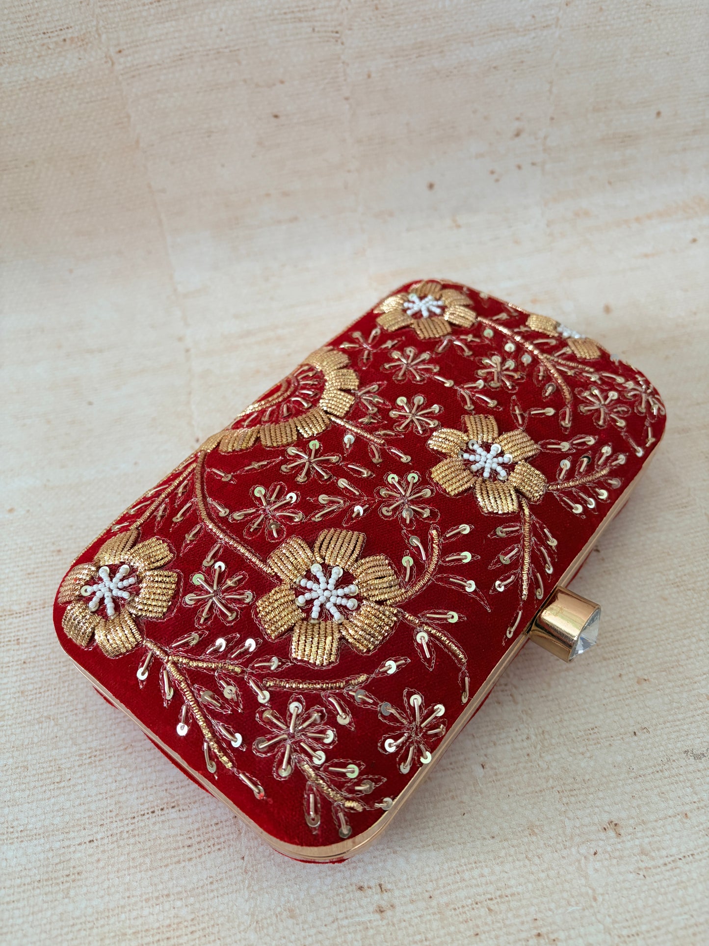Red clutch bag with gold floral embroidery on a beige background