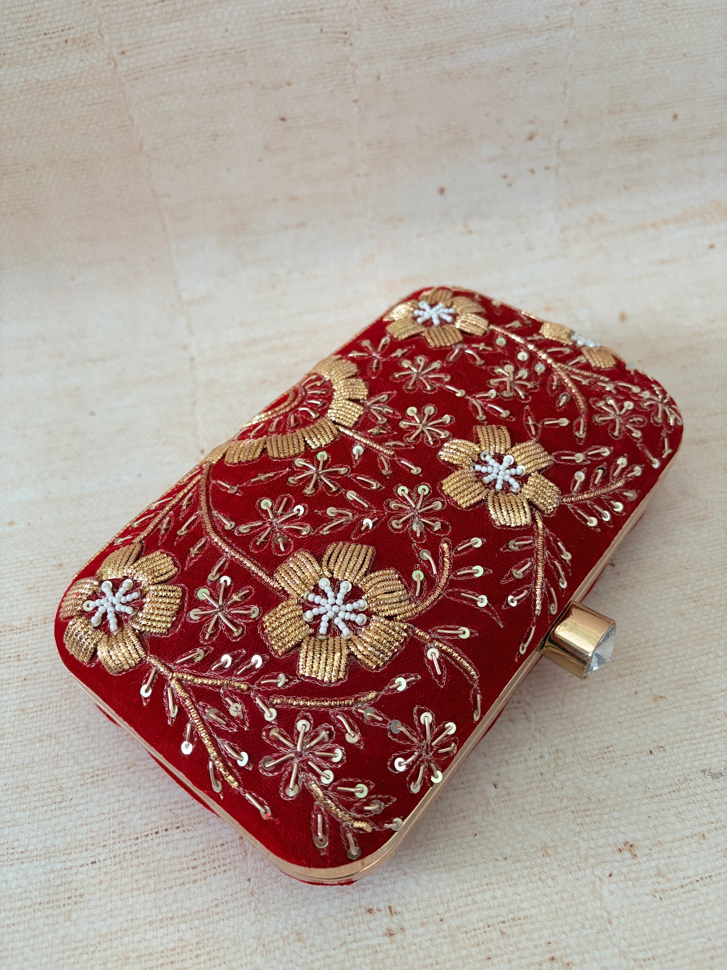 Red clutch bag with gold floral embroidery on a beige background