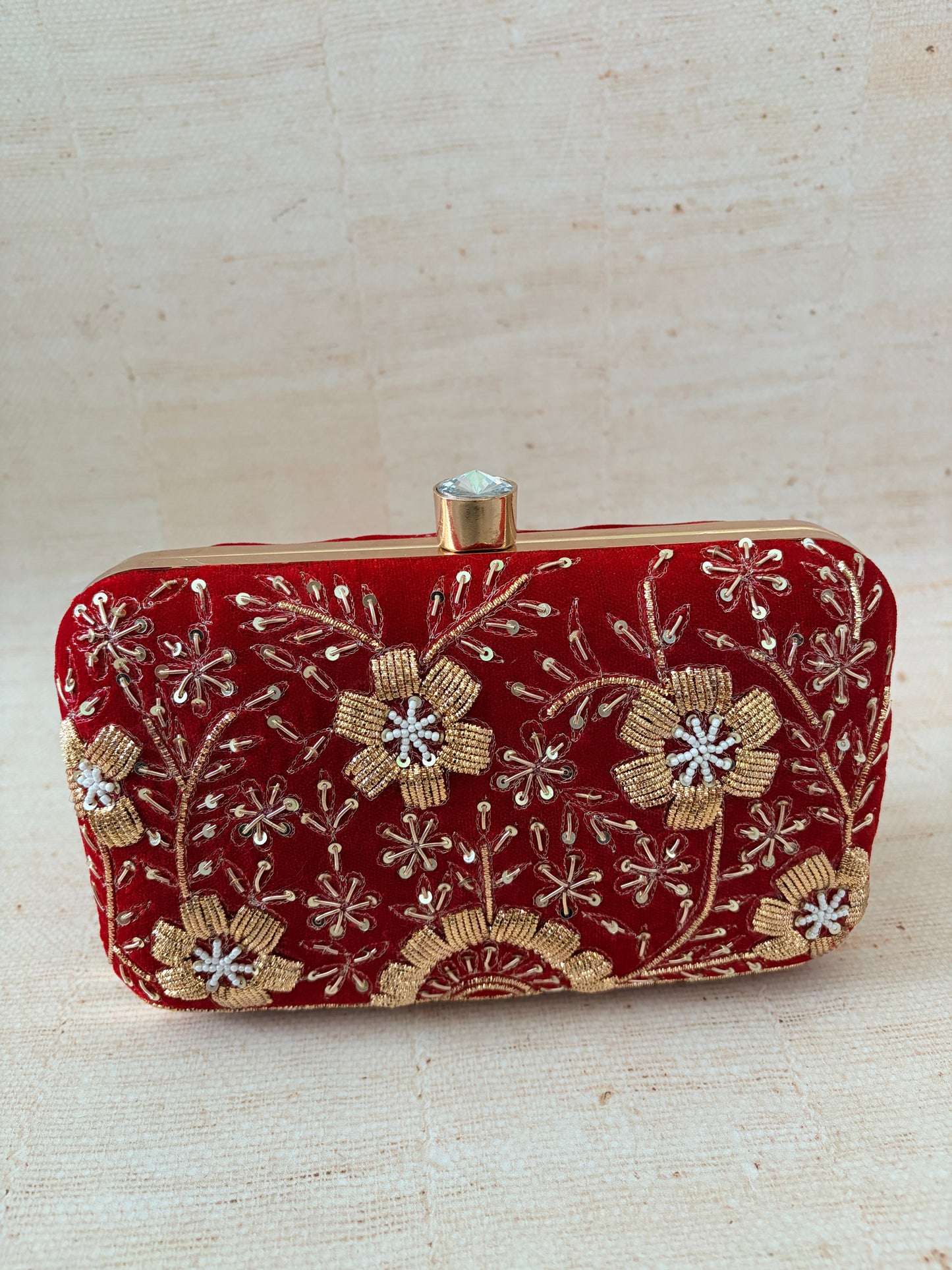 Red clutch with gold floral embroidery on a beige background
