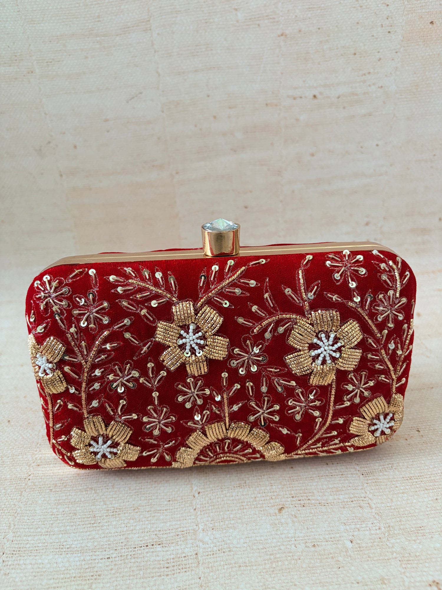 Red clutch with gold floral embroidery on a beige background