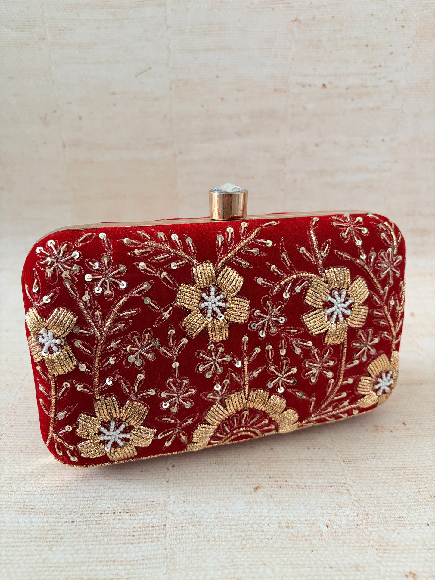 Red embroidered clutch with gold floral patterns on a beige background