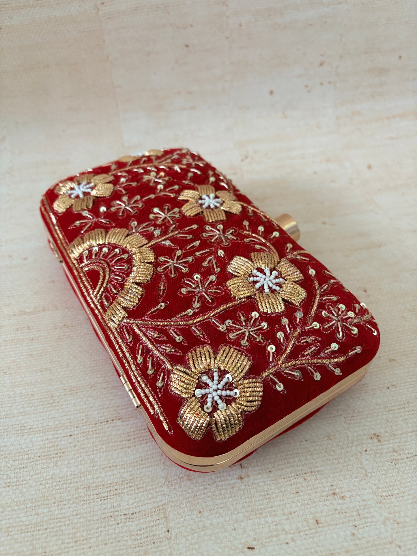 Red pouch with gold floral embroidery on a beige background