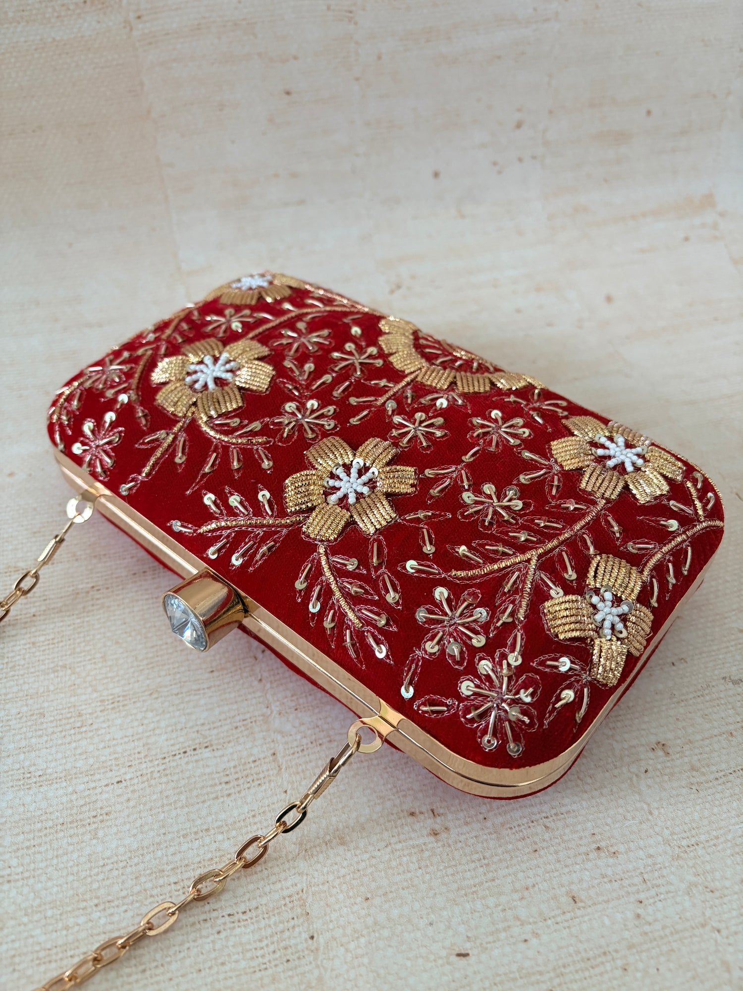 Red clutch bag with gold floral embroidery on a beige background