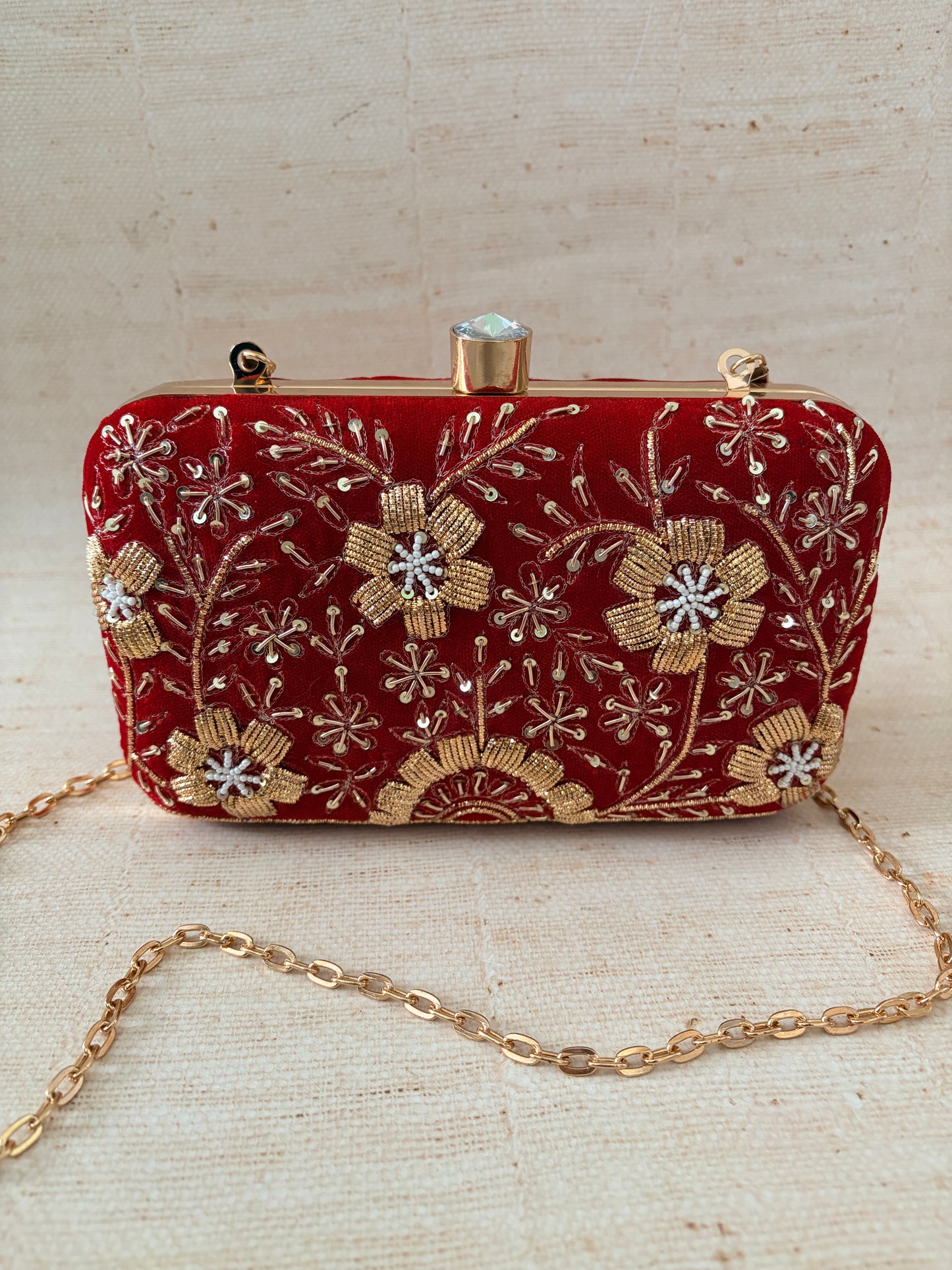 Red embroidered clutch bag with gold chain on a beige background