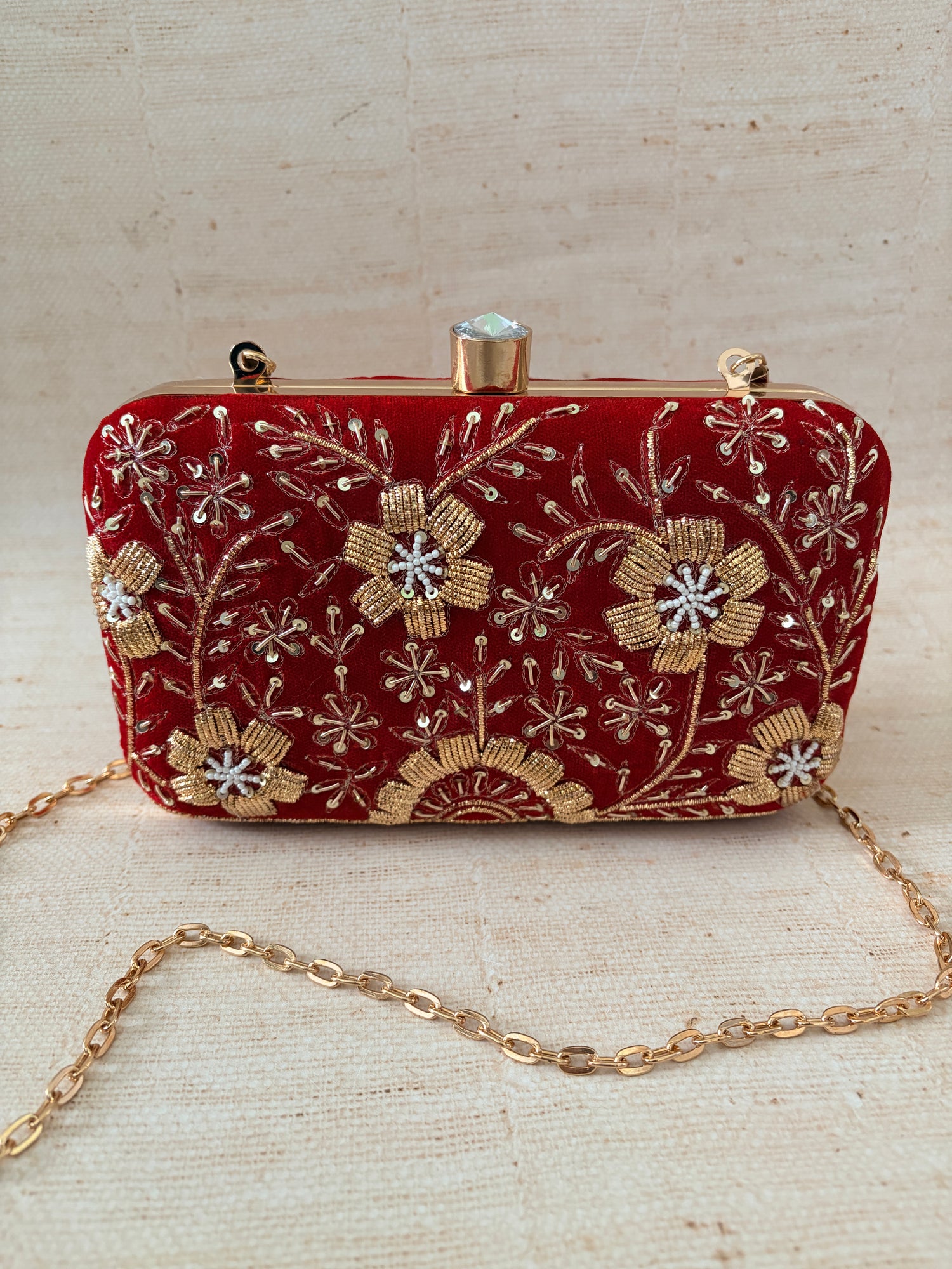 Red embroidered clutch bag with gold chain on a beige background