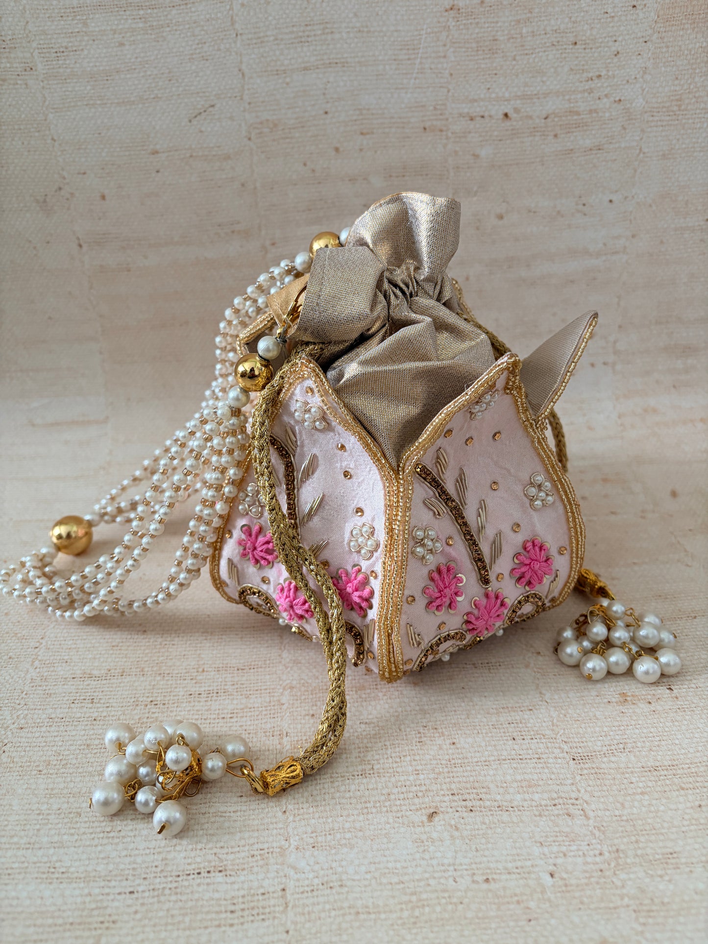 Decorative handbag with floral embroidery and pearl embellishments on a textured beige background