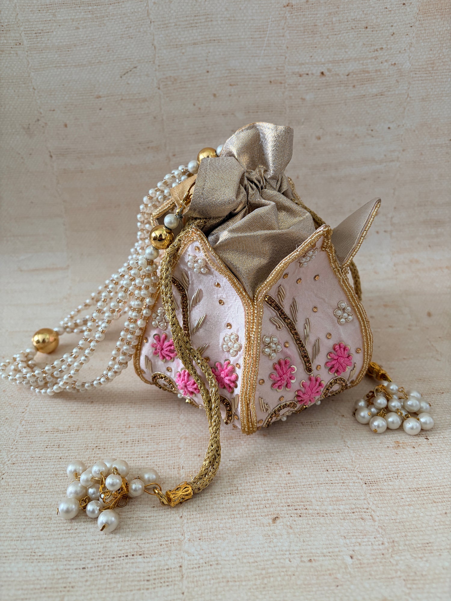 Decorative handbag with floral embroidery and pearl embellishments on a textured beige background