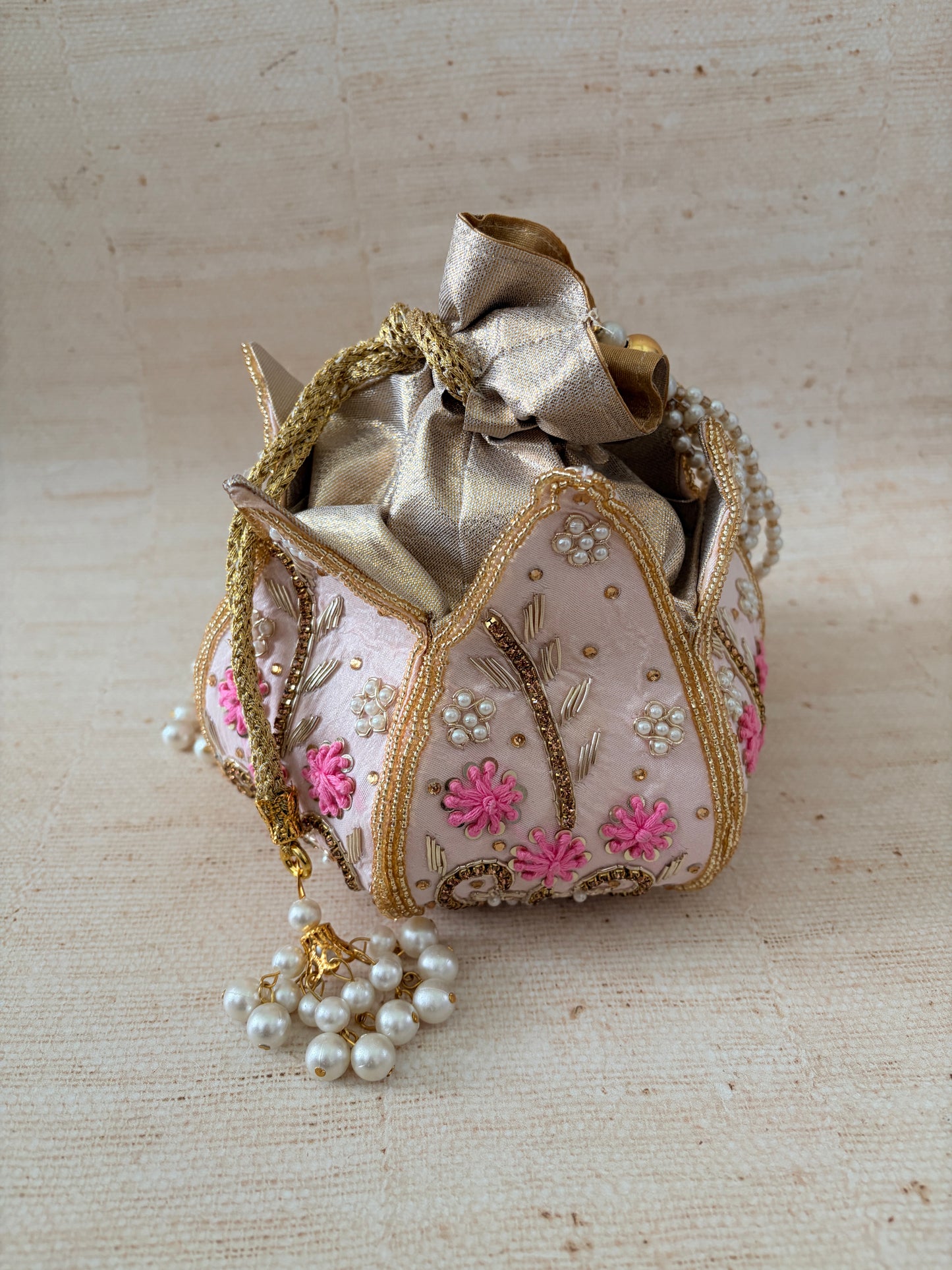 Decorative handbag with floral embroidery and a pearl tassel on a textured beige background