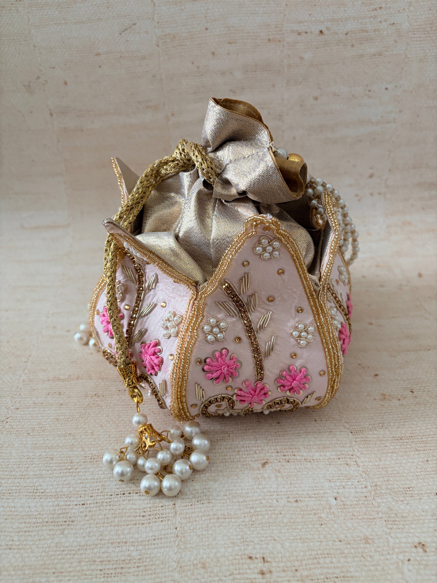 Decorative handbag with floral embroidery and a pearl tassel on a textured beige background