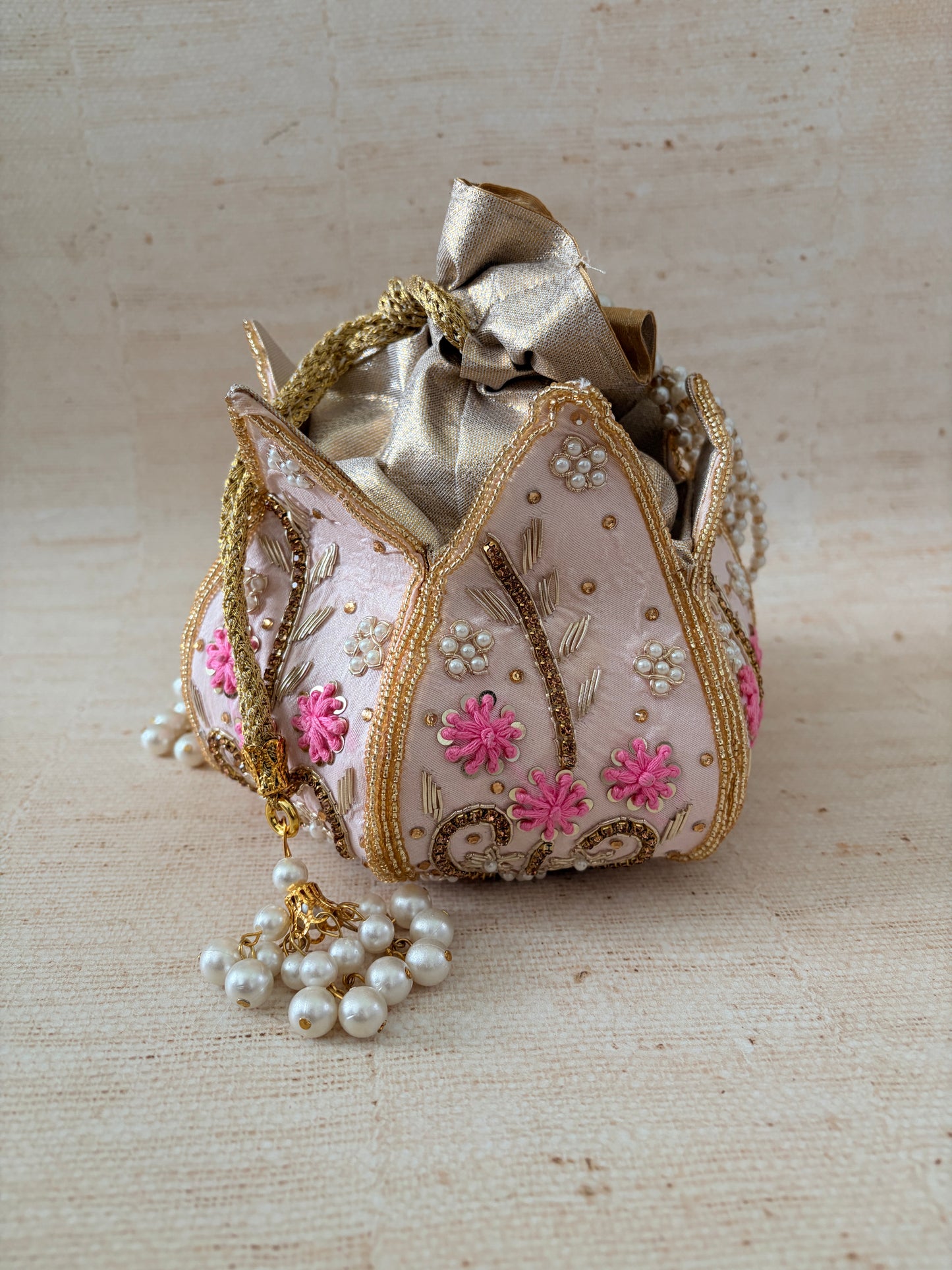 Decorative heart-shaped box with floral embroidery and a pearl necklace on a textured beige background