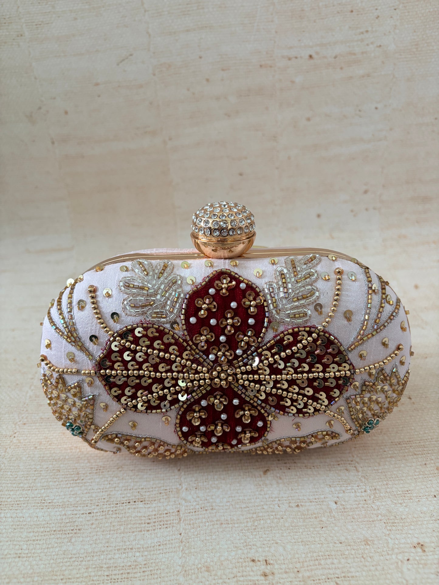 Decorative clutch bag with floral design and embellishments on a beige background