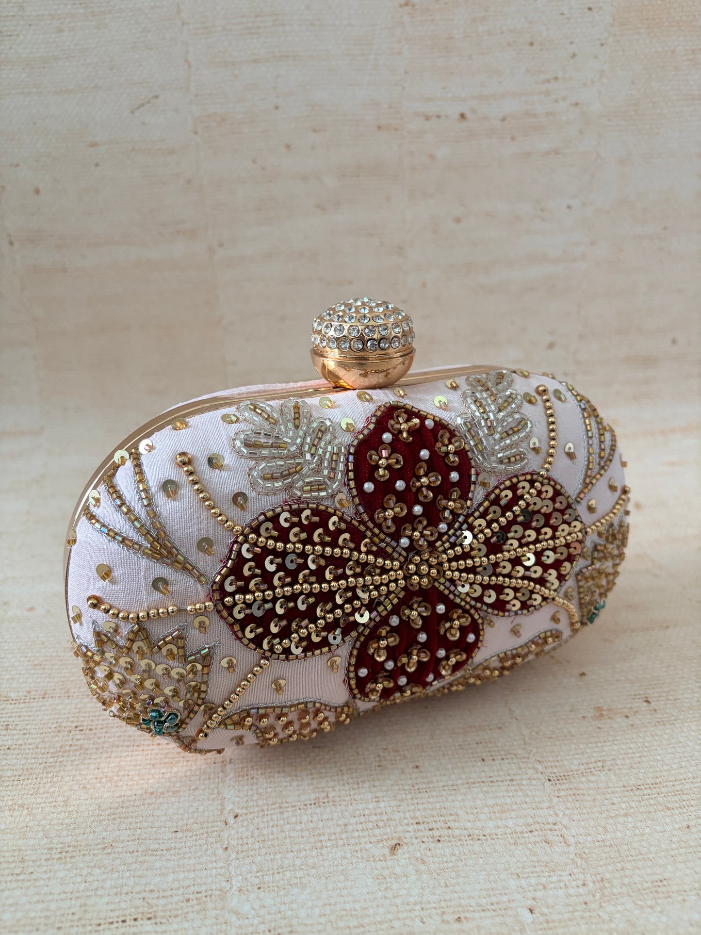 Decorative clutch with floral design and embellishments on a beige background