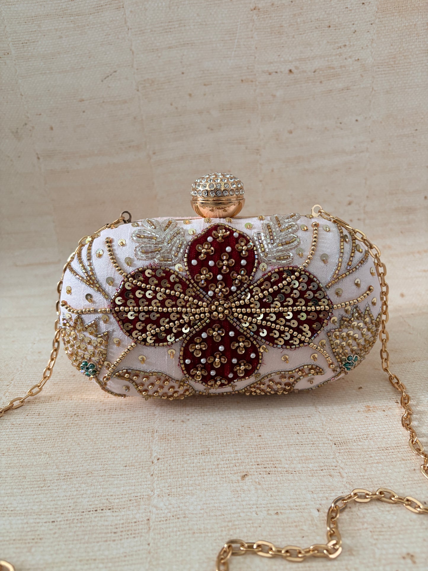 Elegant clutch bag with floral design and gold chain on a textured beige background