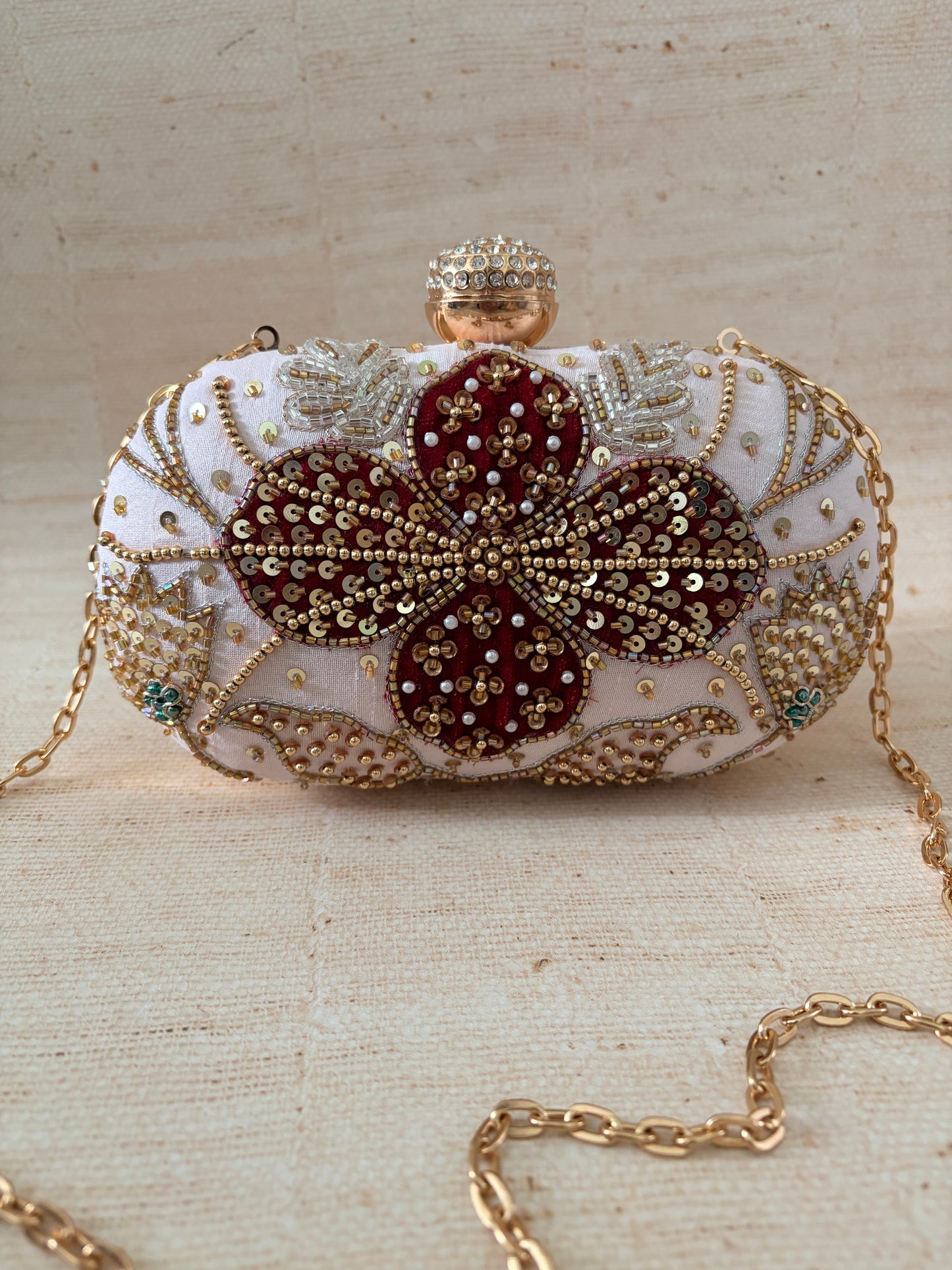 Decorative clutch with intricate gold and red design on a beige background