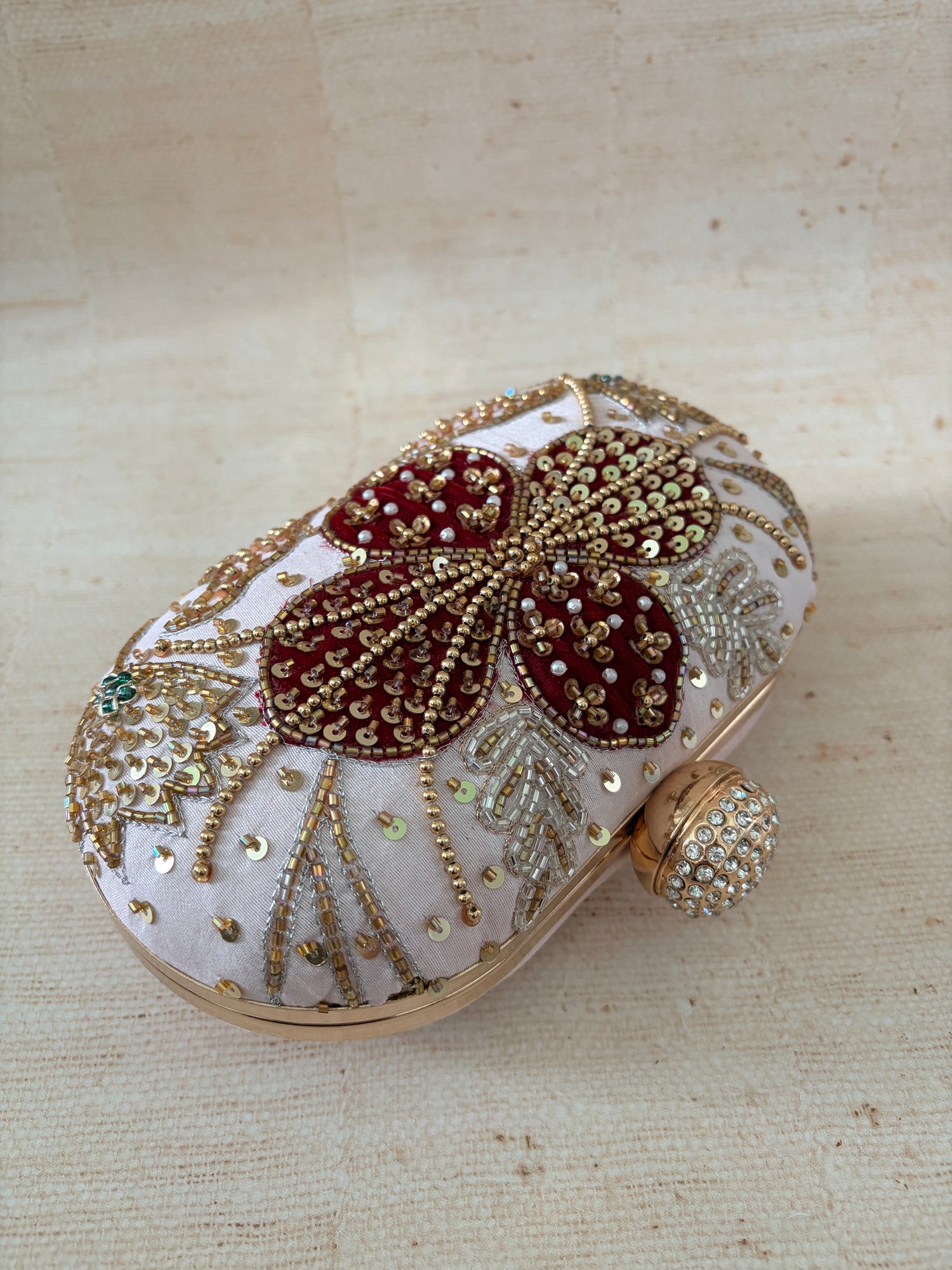 Decorative clutch with intricate gold and red patterns on a beige background