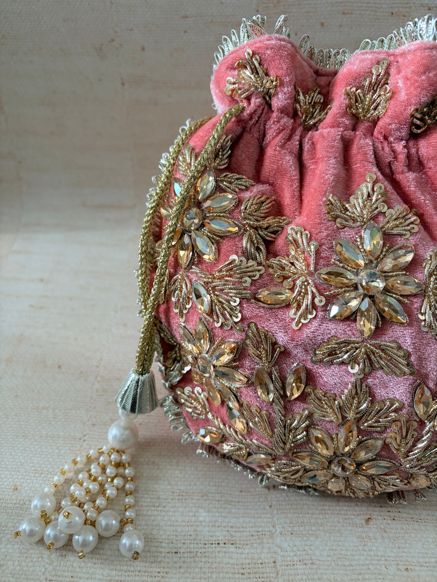 Pink fabric with gold embroidery and a pearl necklace on a beige background