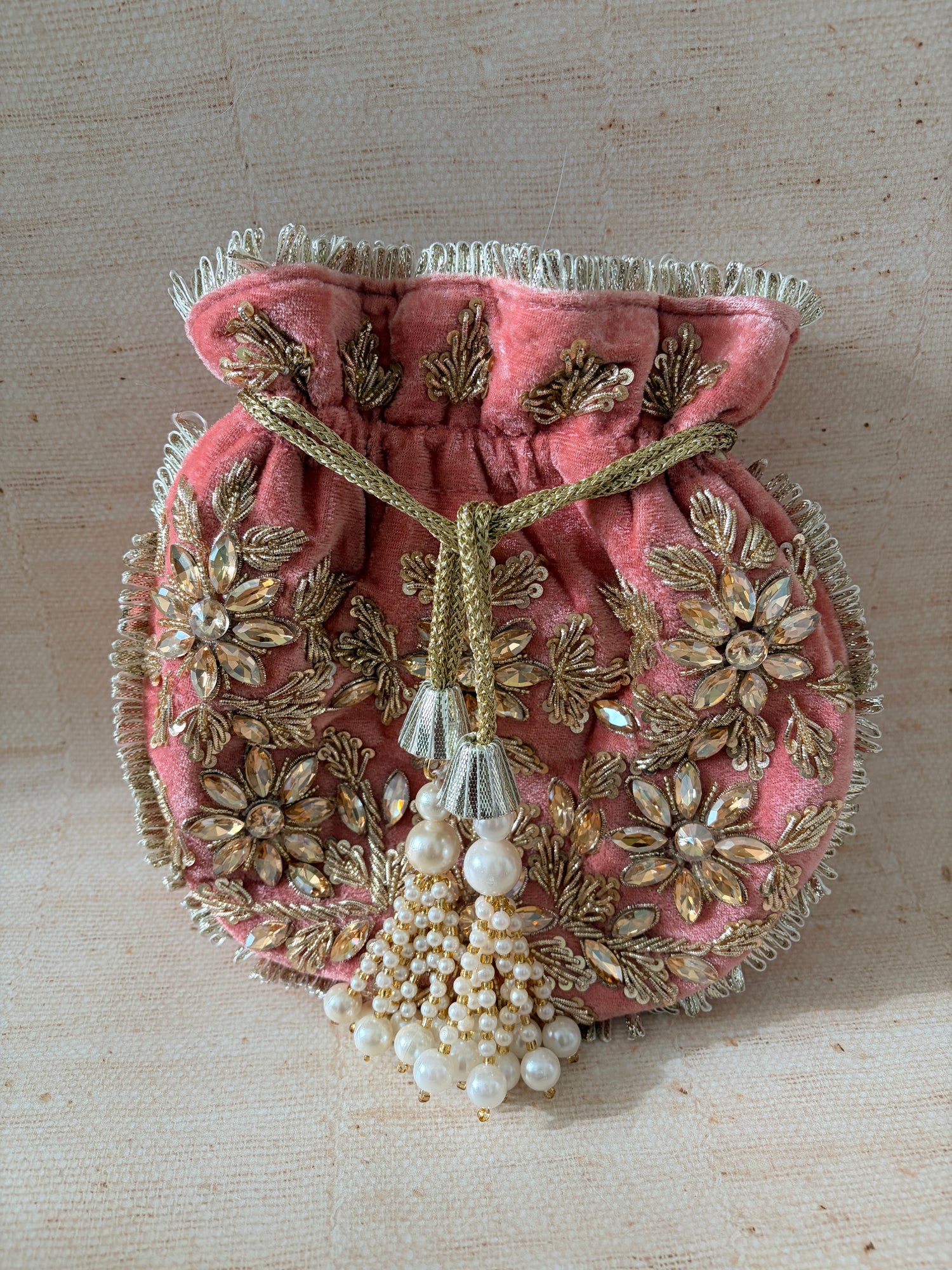 Decorative pink fabric with gold embroidery and pearl embellishments on a beige background