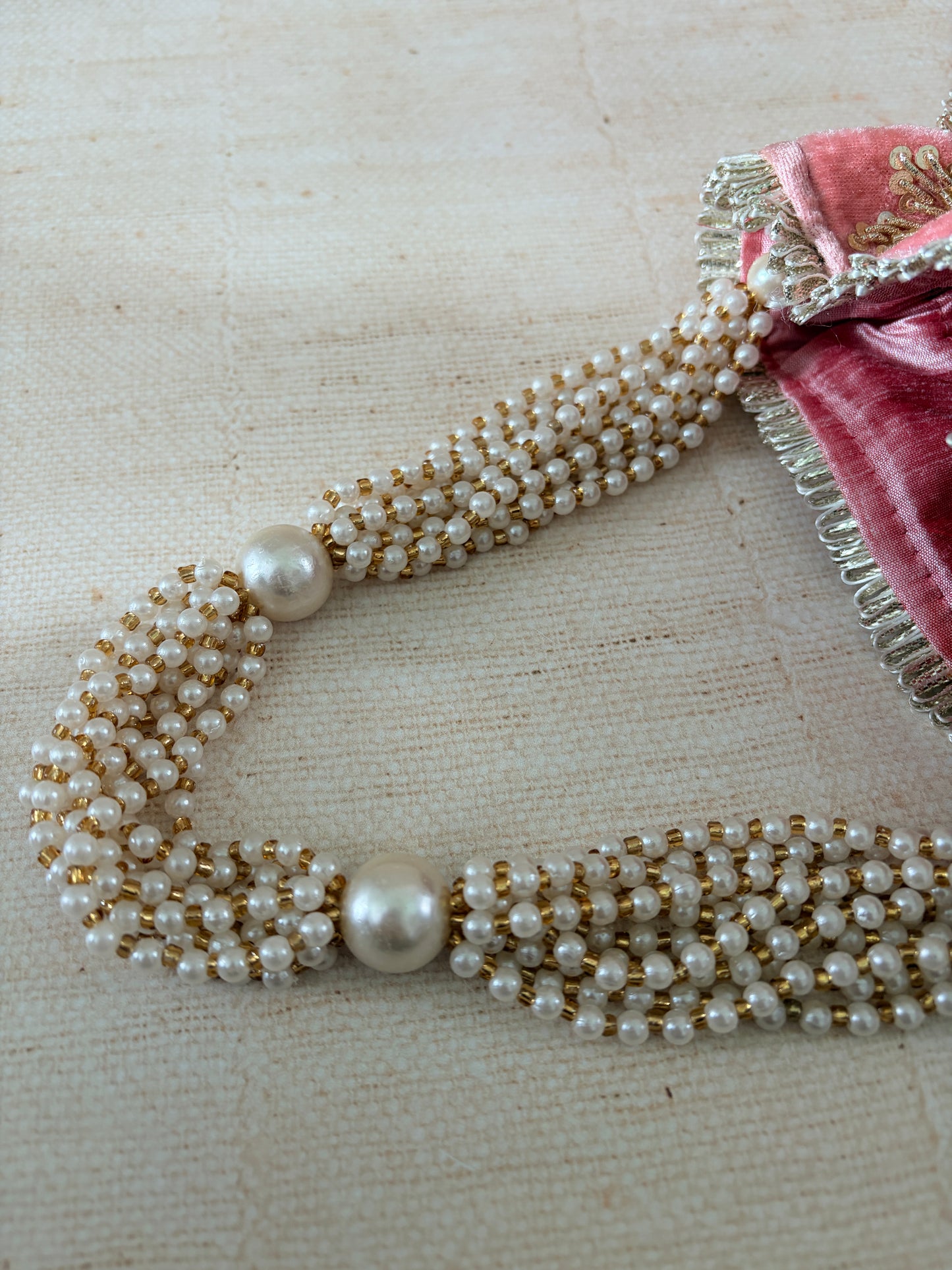 Pearl necklace with gold accents on a textured beige background