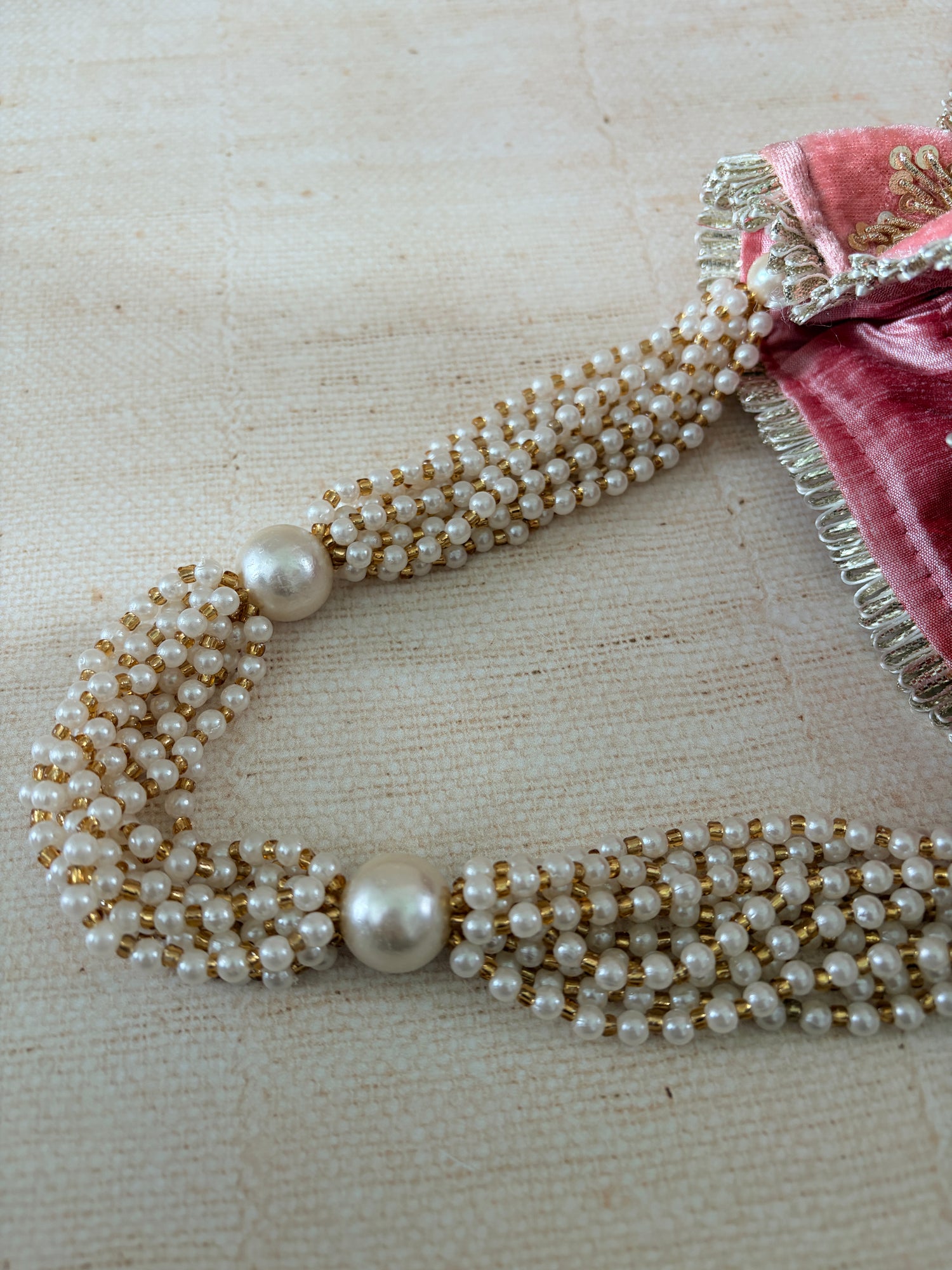 Pearl necklace with gold accents on a textured beige background