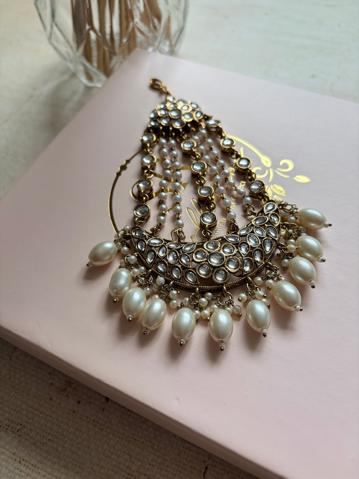 Pearl and gold brooch on a pink card with a decorative design.