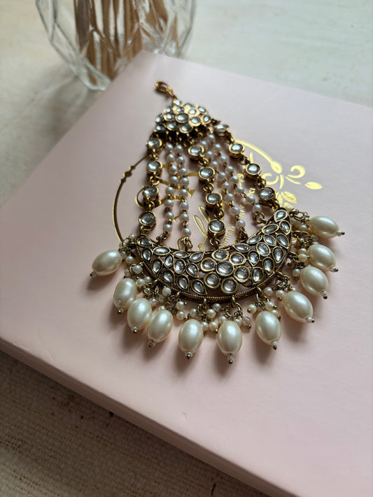 Pearl and gold brooch on a pink card with a decorative design.