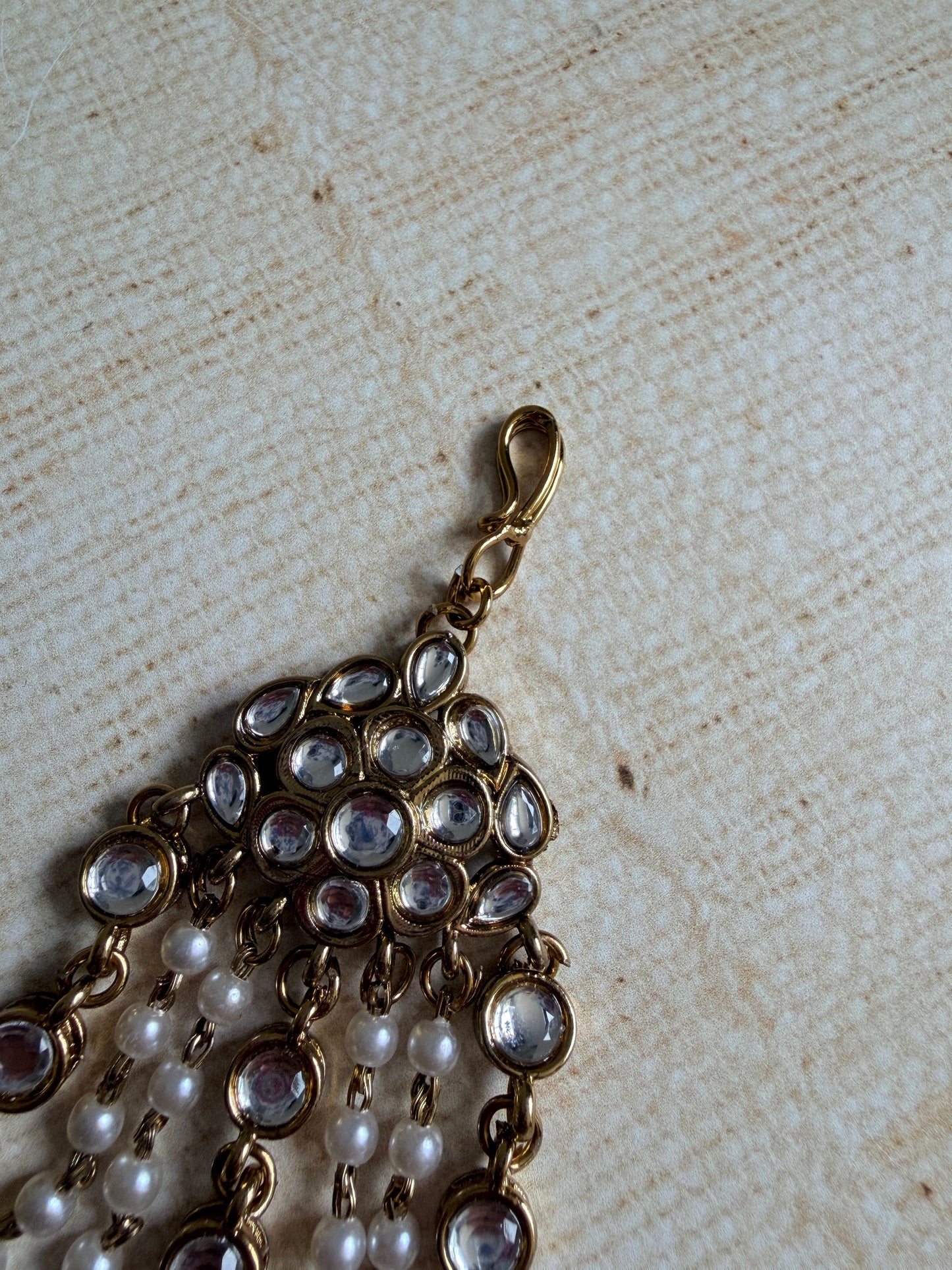 Close-up of a gold necklace with pearls and crystals on a textured beige background