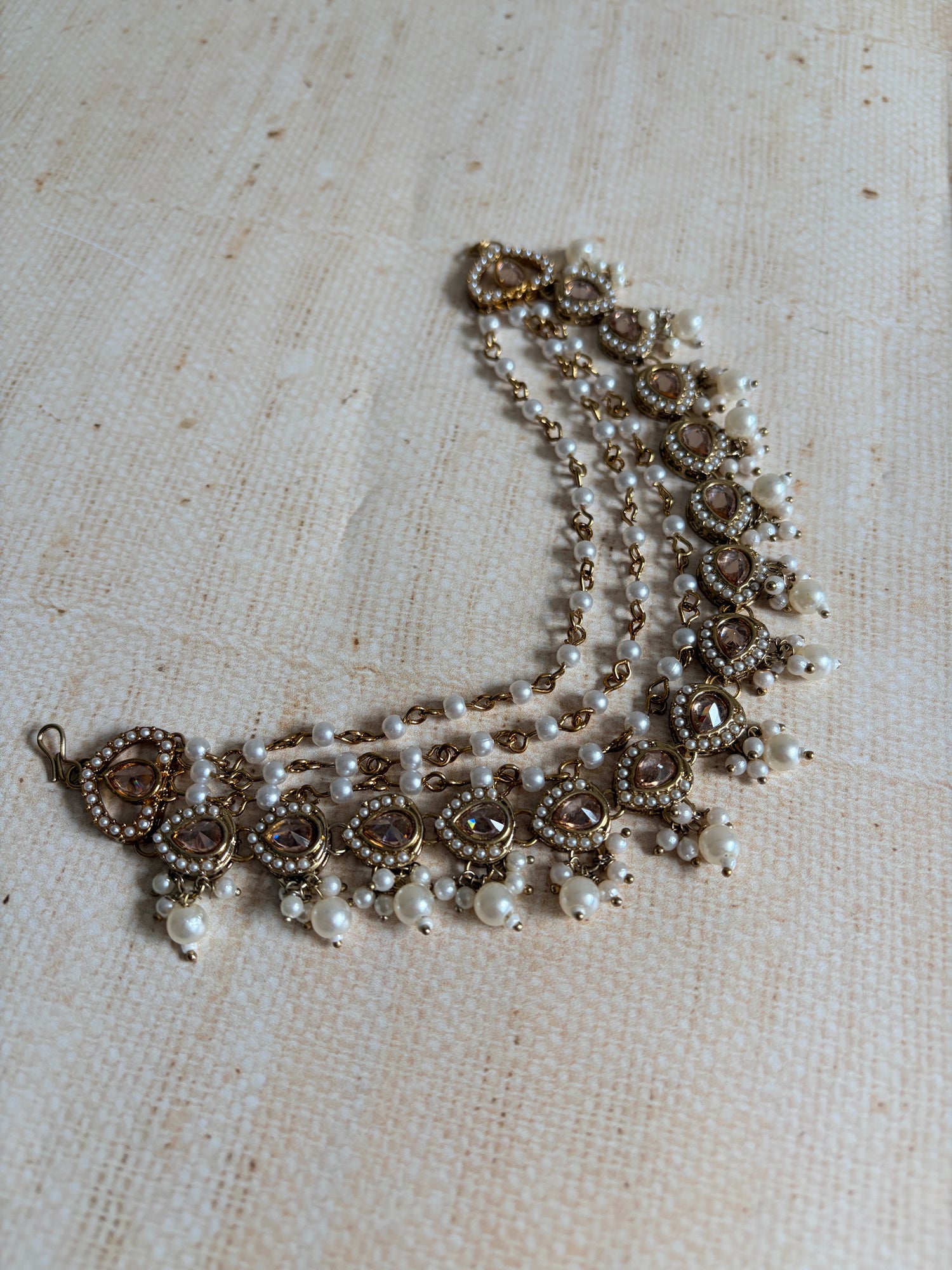 Pearl and gold necklace on a textured beige fabric background