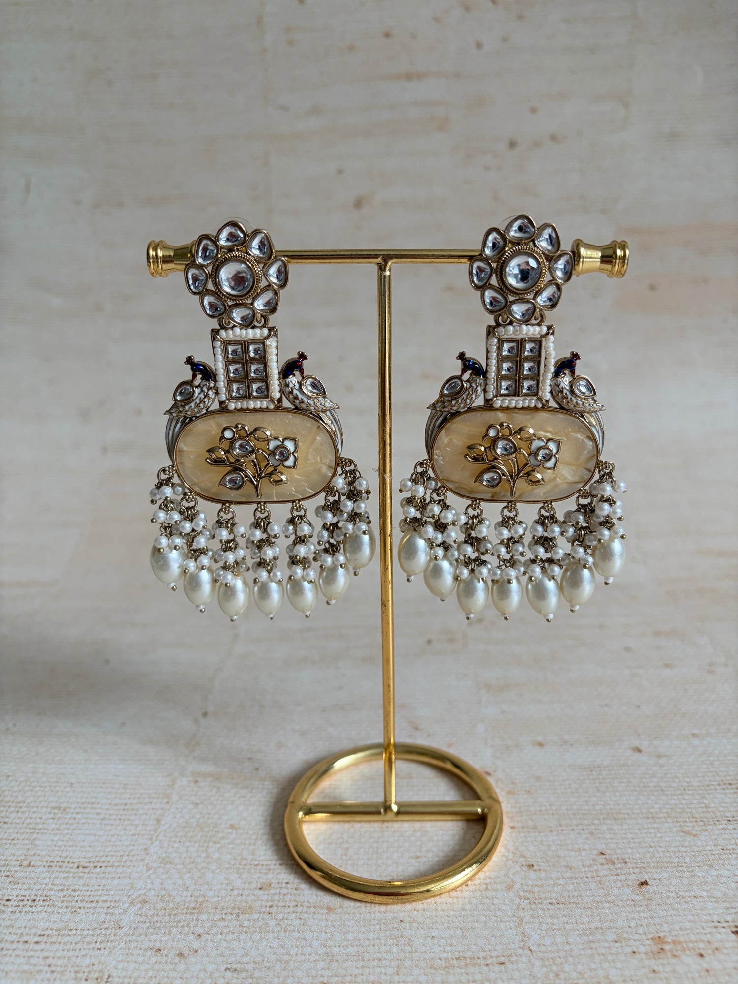 Pair of ornate earrings with gold and silver details on a textured beige background