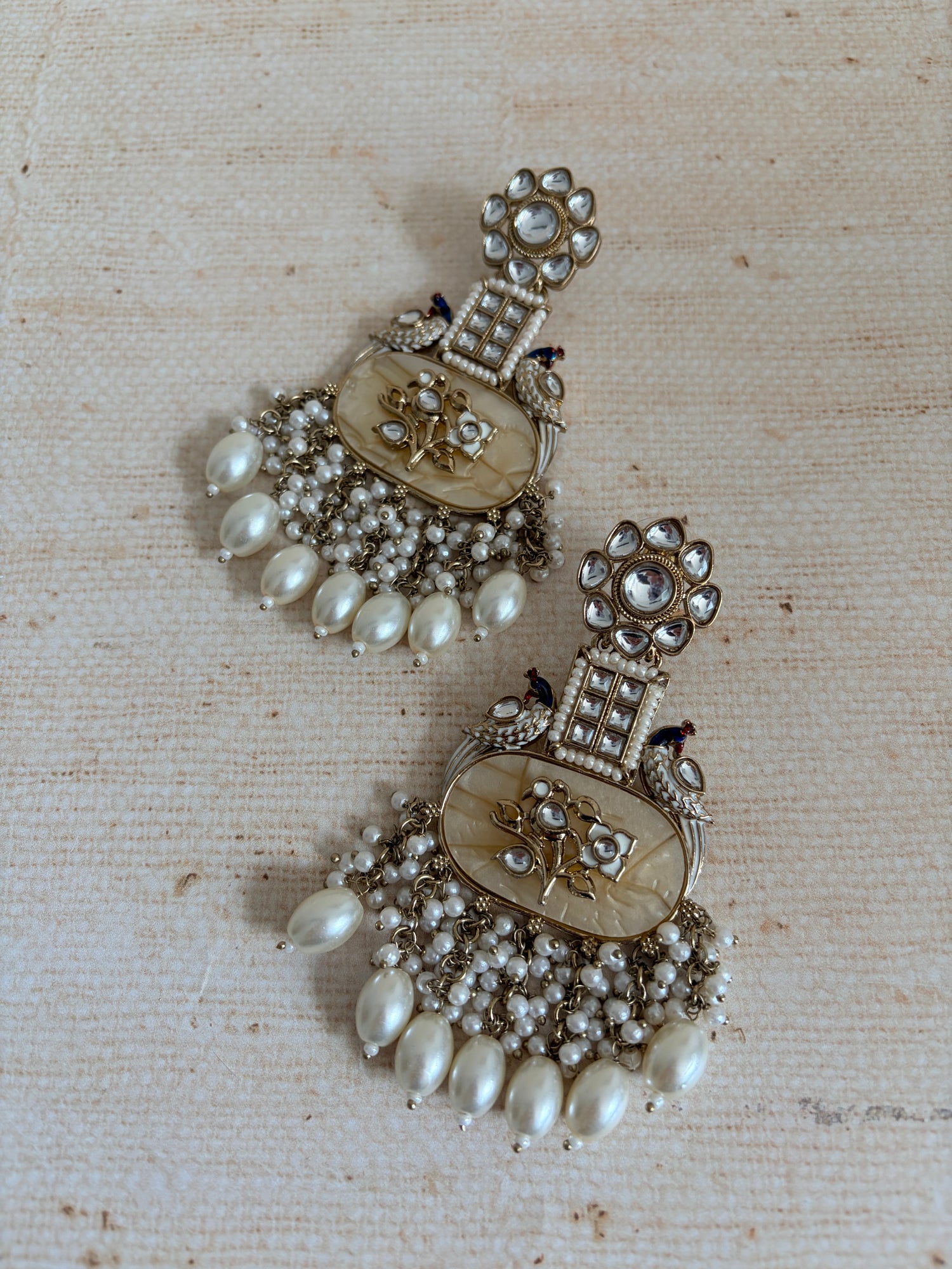 Pair of ornate earrings with pearls on a textured beige background