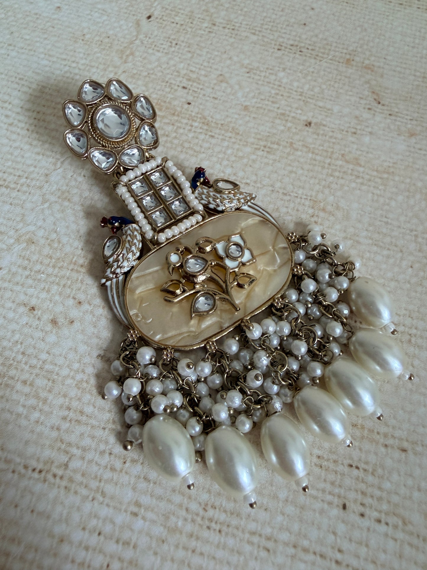 Vintage-style brooch with pearls and intricate design on a textured fabric background