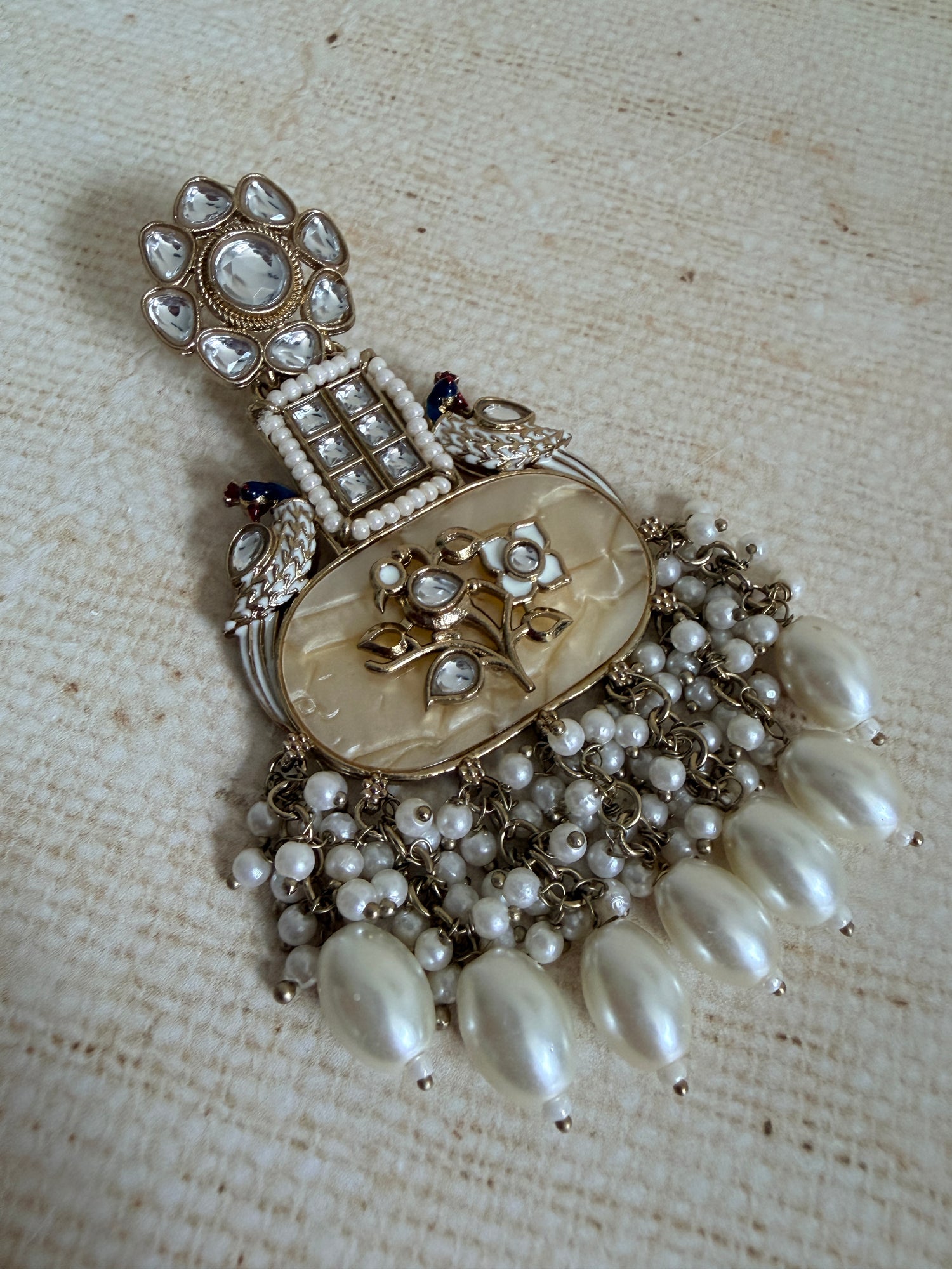 Vintage-style brooch with pearls and intricate design on a textured fabric background
