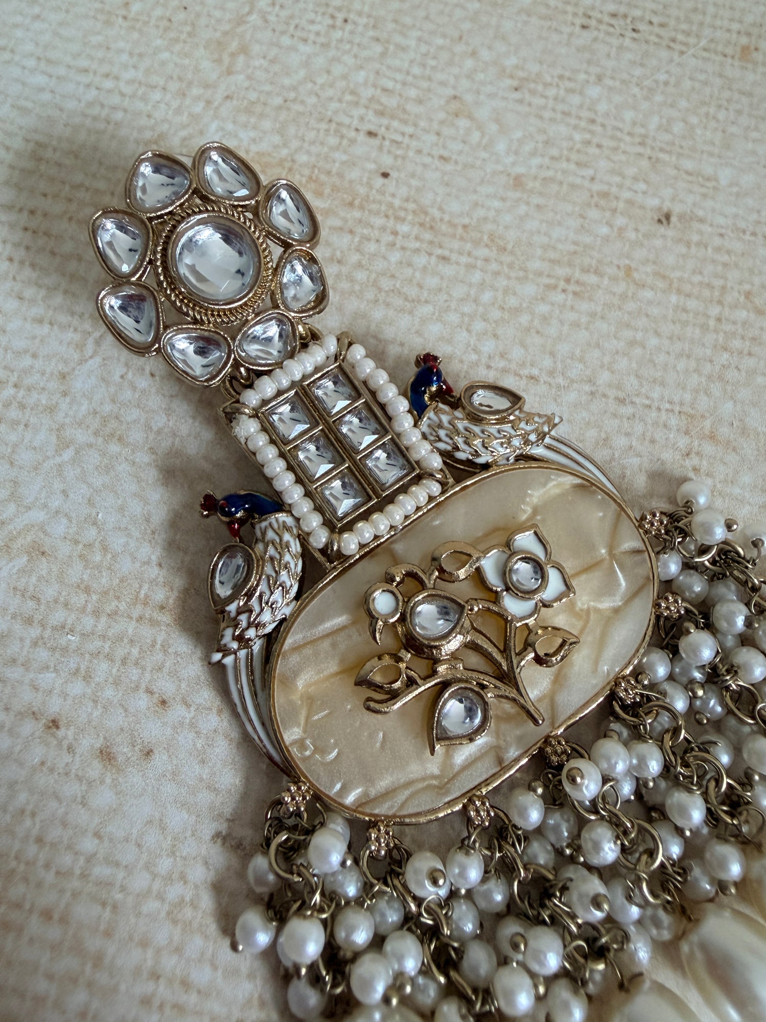 Vintage-style necklace with intricate design and pearl accents on a textured beige background