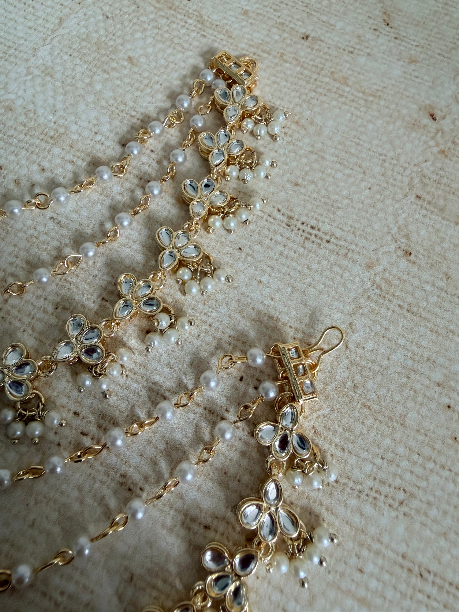 Gold and pearl jewelry set on a textured beige surface