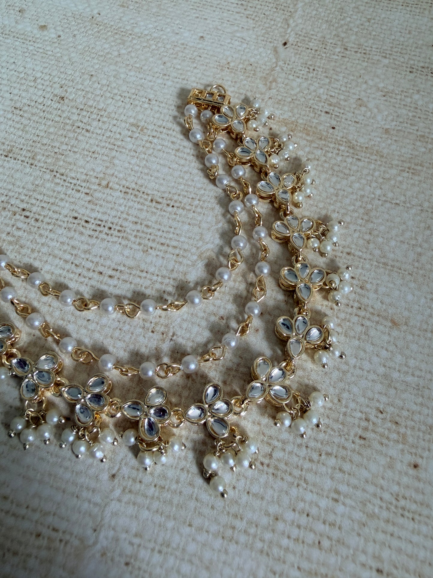 Pearl and gold necklace on a textured beige fabric background