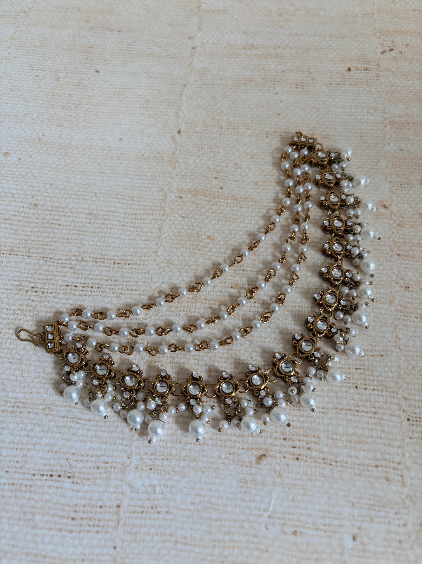 Pearl and gold beaded necklace on a textured beige fabric background
