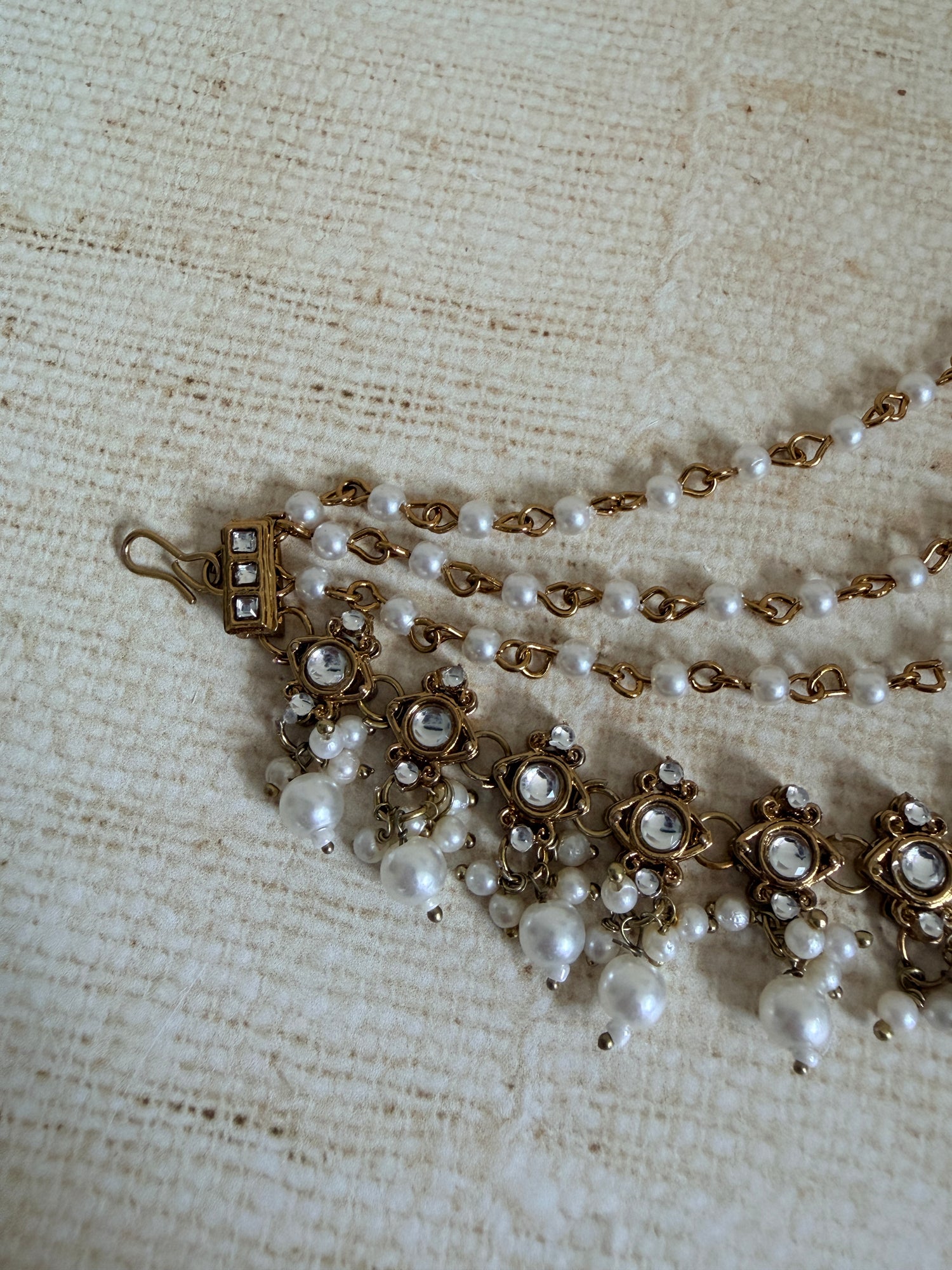 Pearl necklace with gold clasps on a textured beige fabric background
