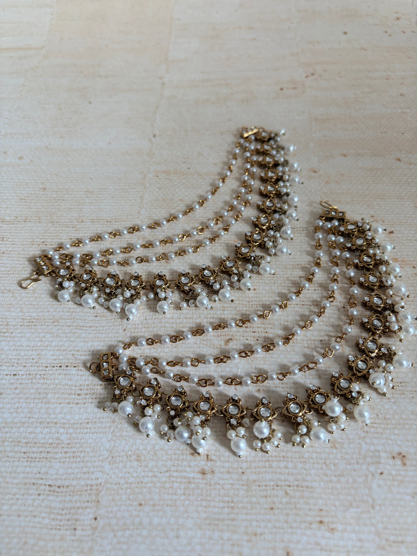 Set of pearl and gold beaded necklaces on a textured beige background