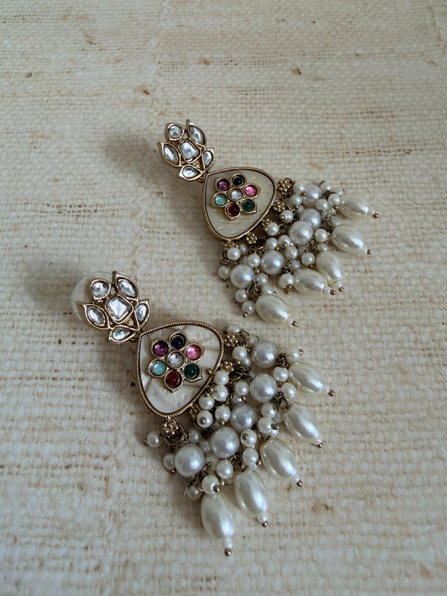 Pair of ornate earrings with pearls and gemstones on a textured beige background