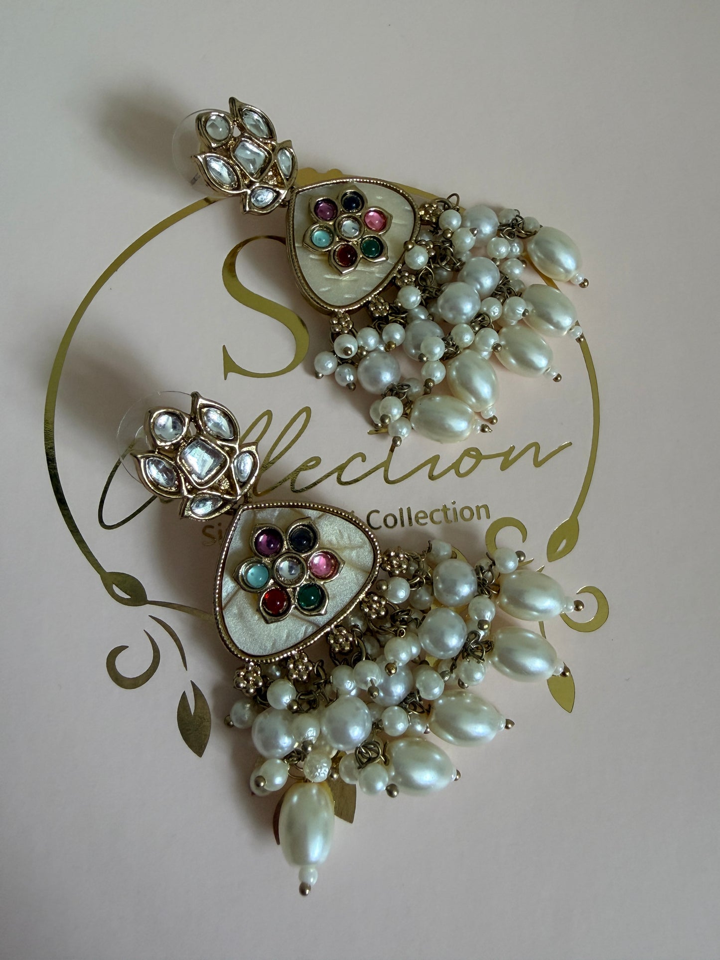 Decorative brooch with pearls and gemstones on a pink background with 'SR Collection' branding.