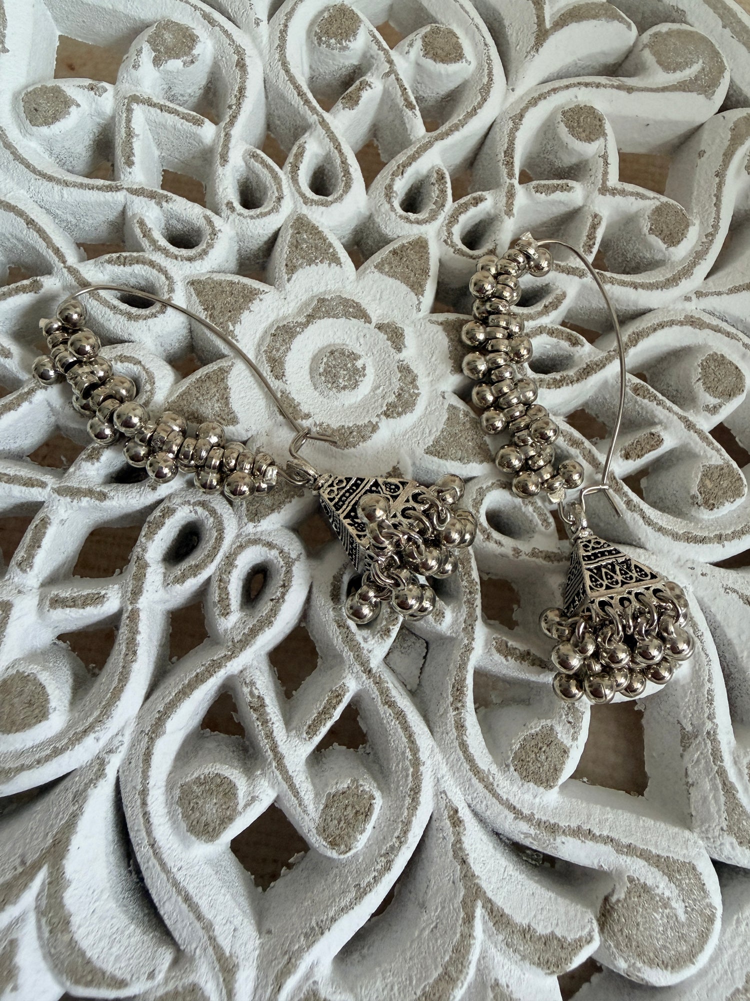 Pair of silver earrings on a decorative white surface with intricate patterns