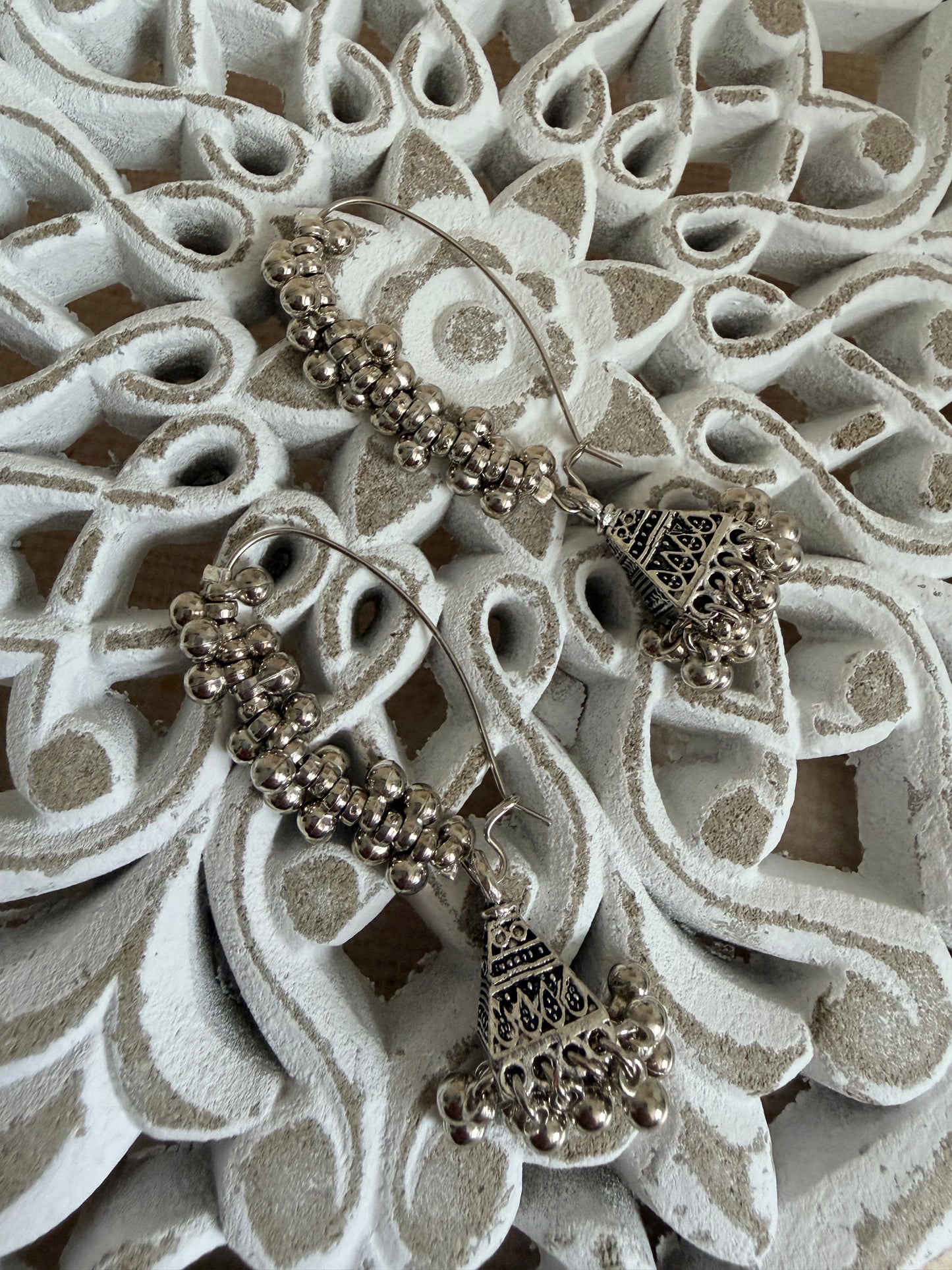 Pair of silver earrings with intricate designs on a decorative white surface