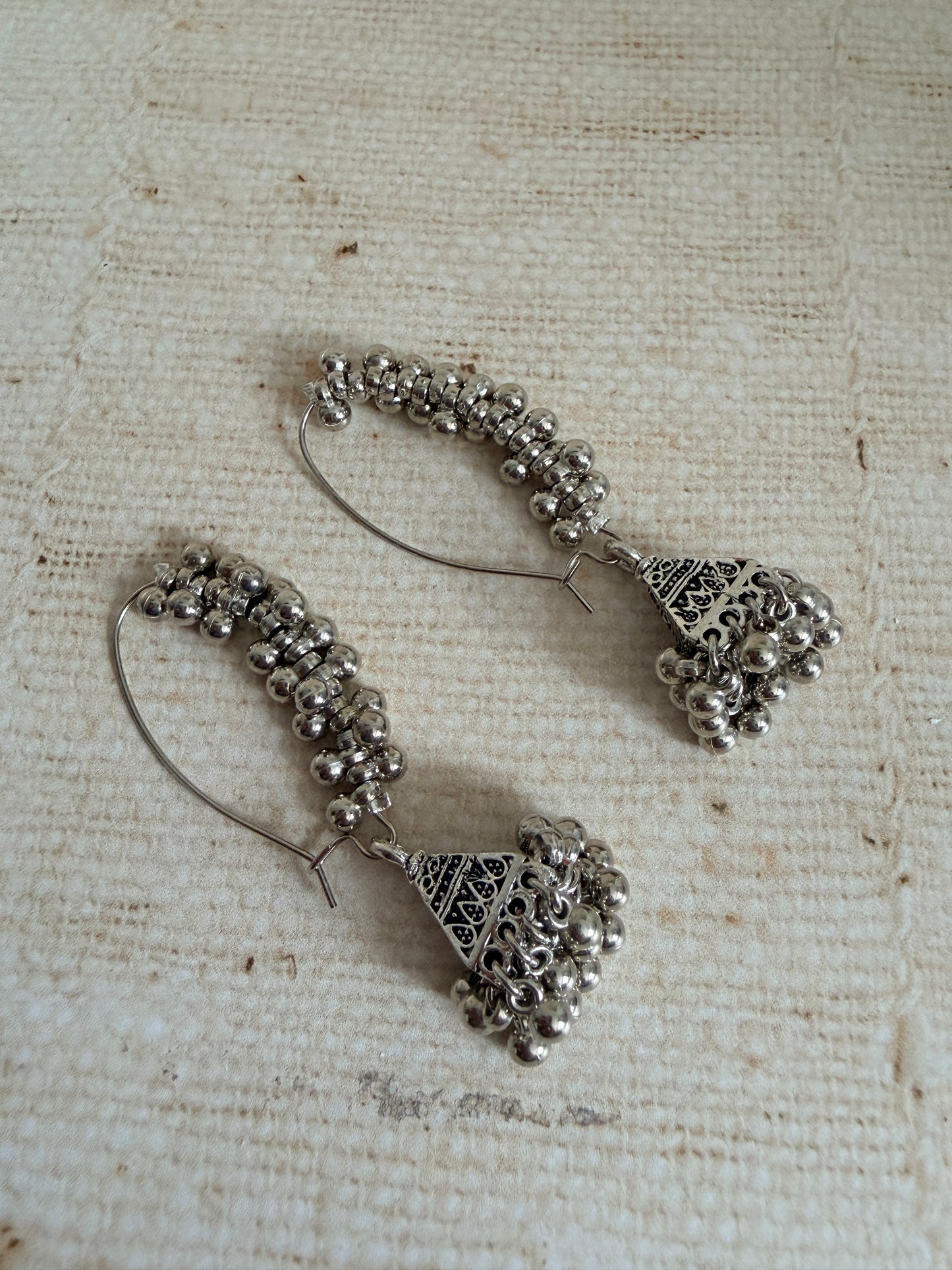 Pair of silver hoop earrings with bead detailing on a textured beige background