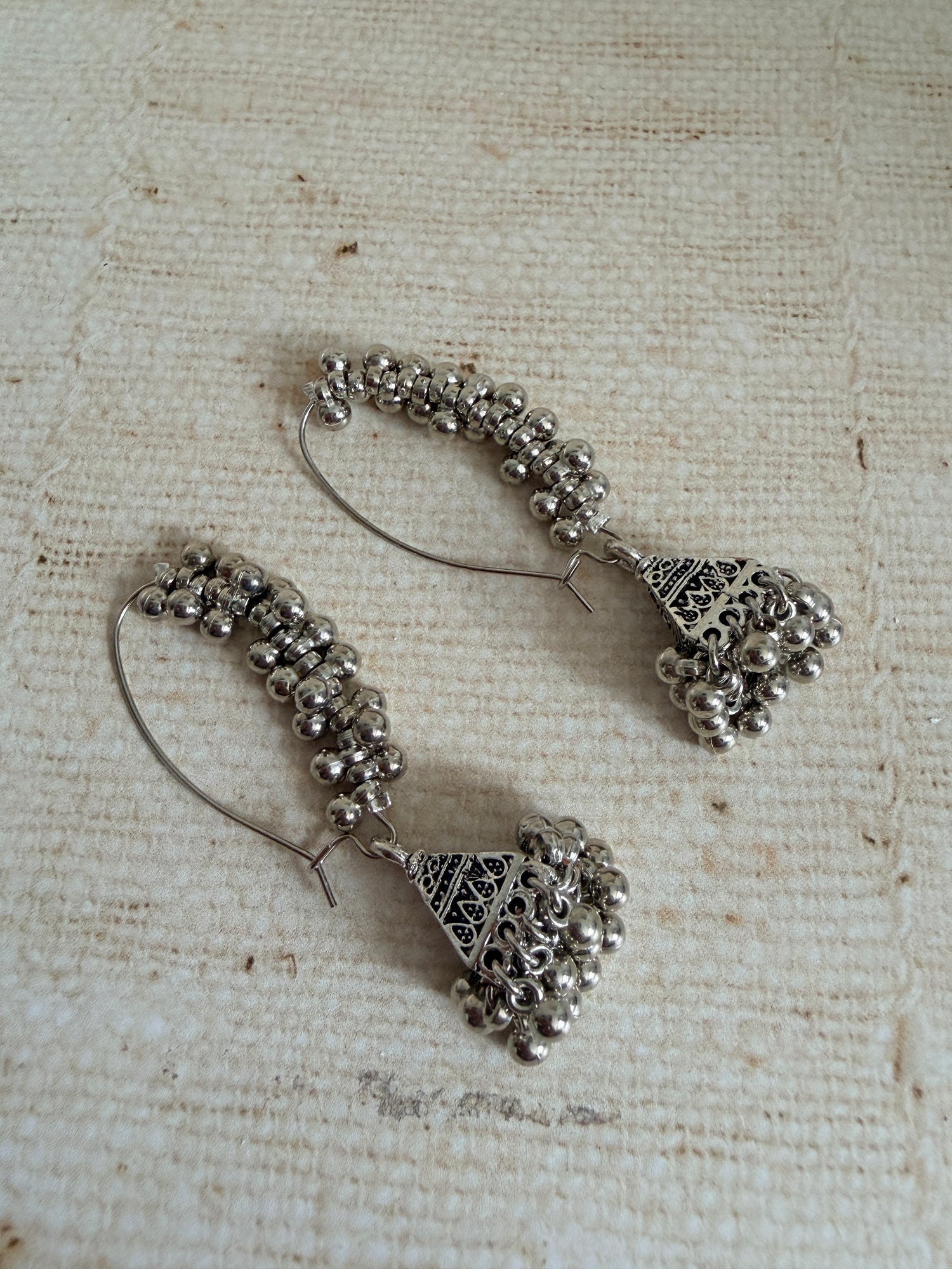 Pair of silver hoop earrings with bead detailing on a textured beige background