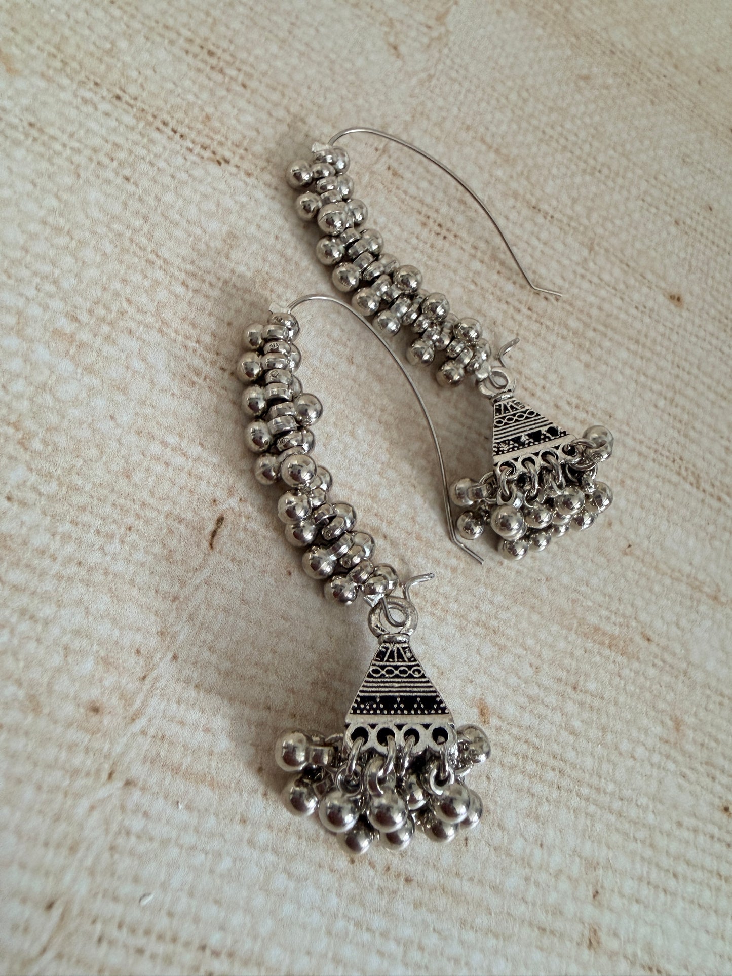Pair of silver hoop earrings with bead detailing on a textured beige surface