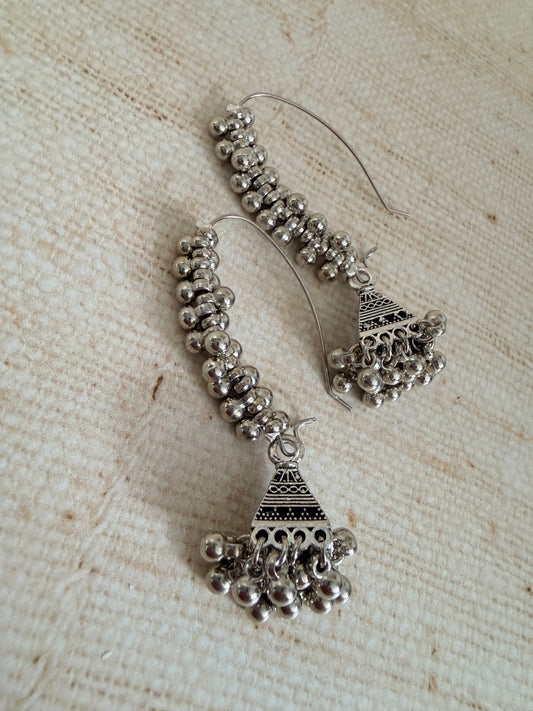 Pair of silver hoop earrings with bead detailing on a textured beige surface