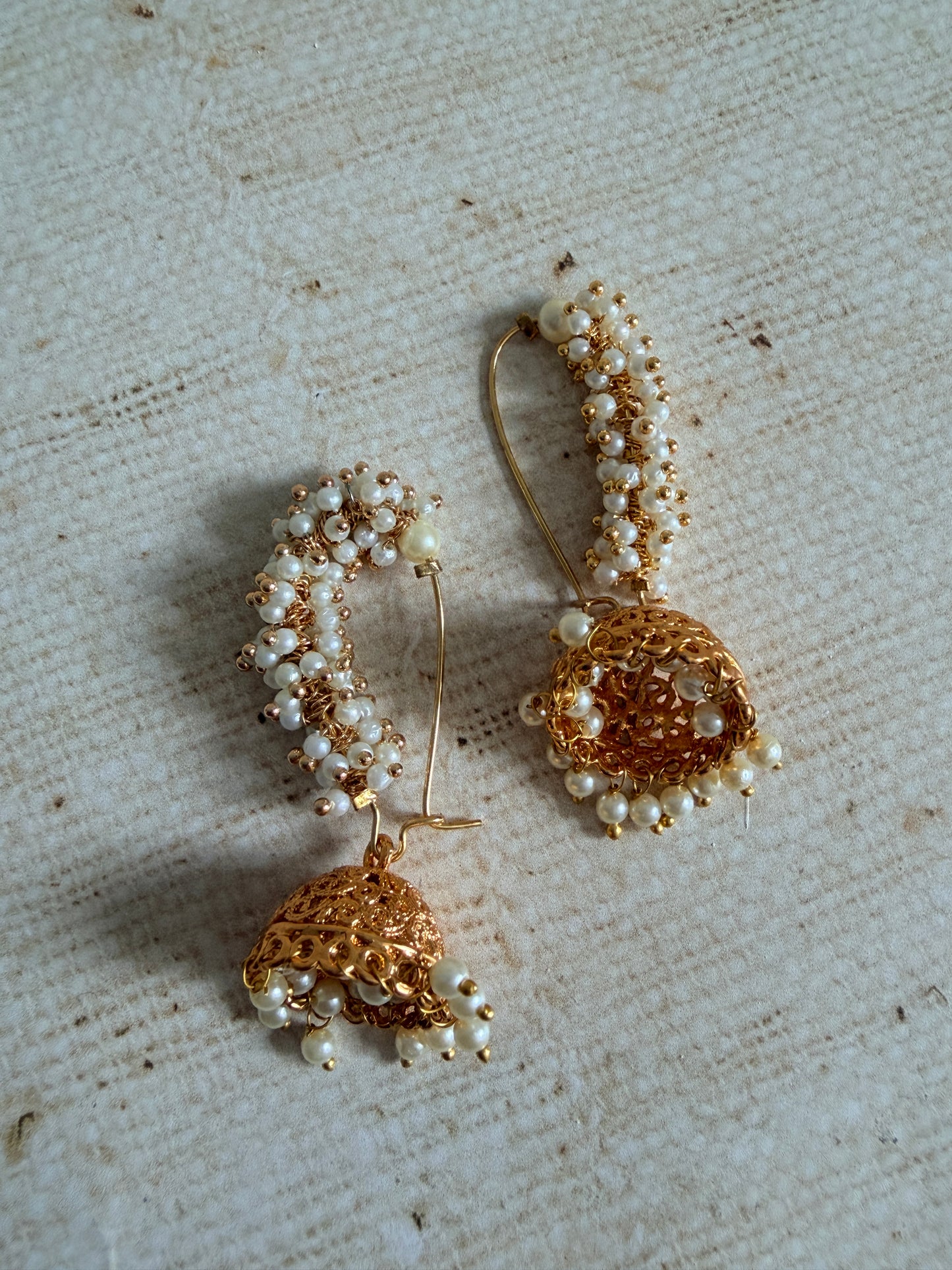 Pair of gold and pearl earrings on a textured fabric background