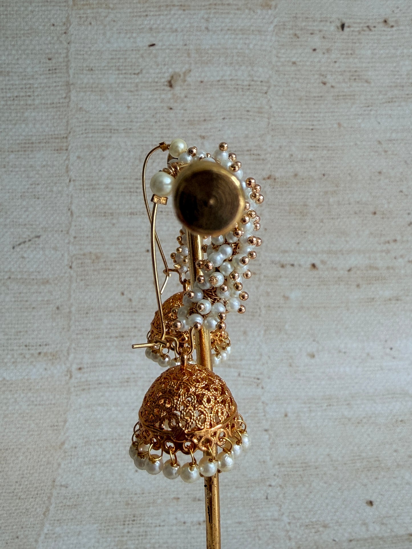 Gold and pearl decorative item on a textured beige background