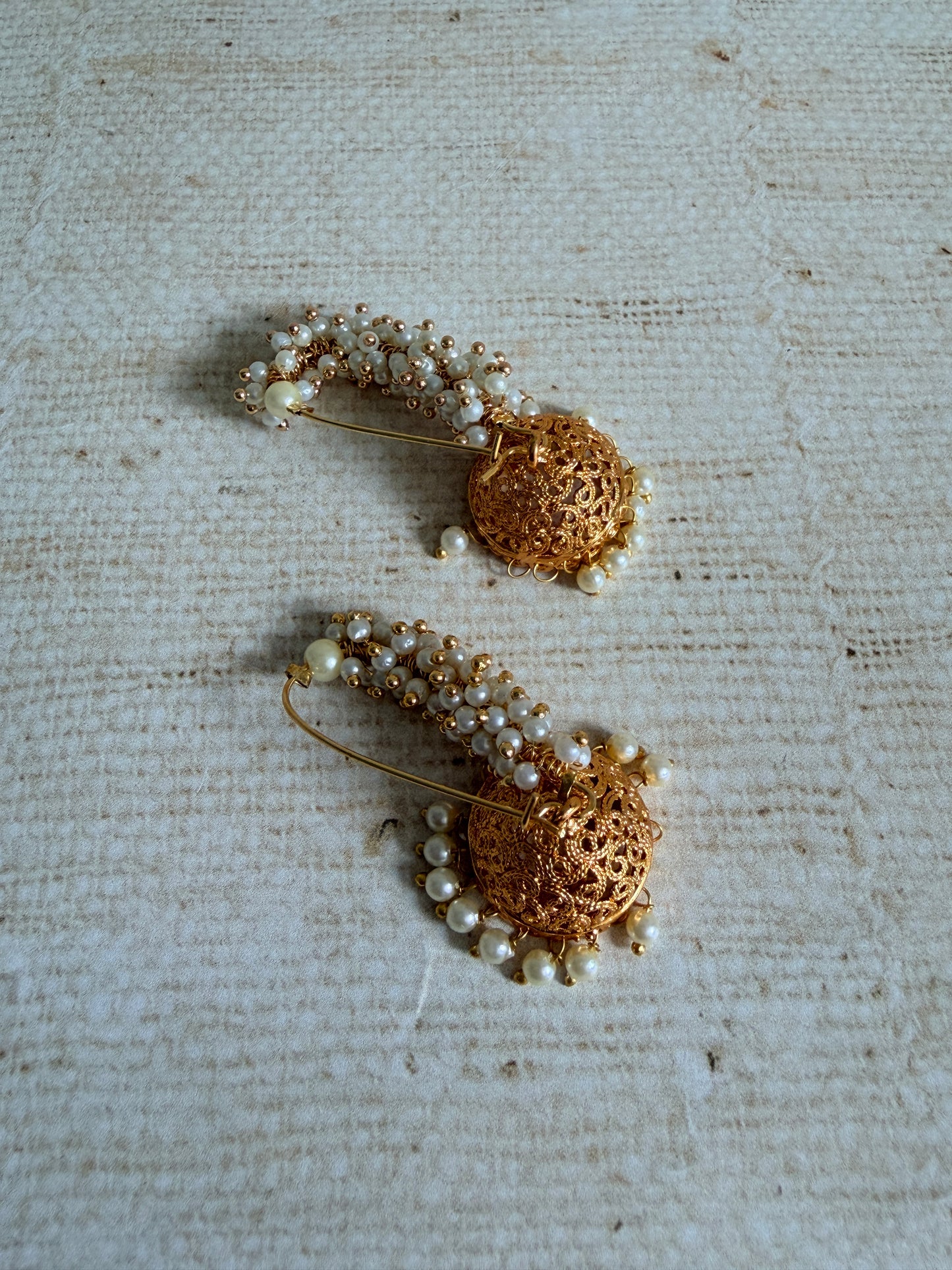 Pair of gold and pearl earrings on a textured beige background