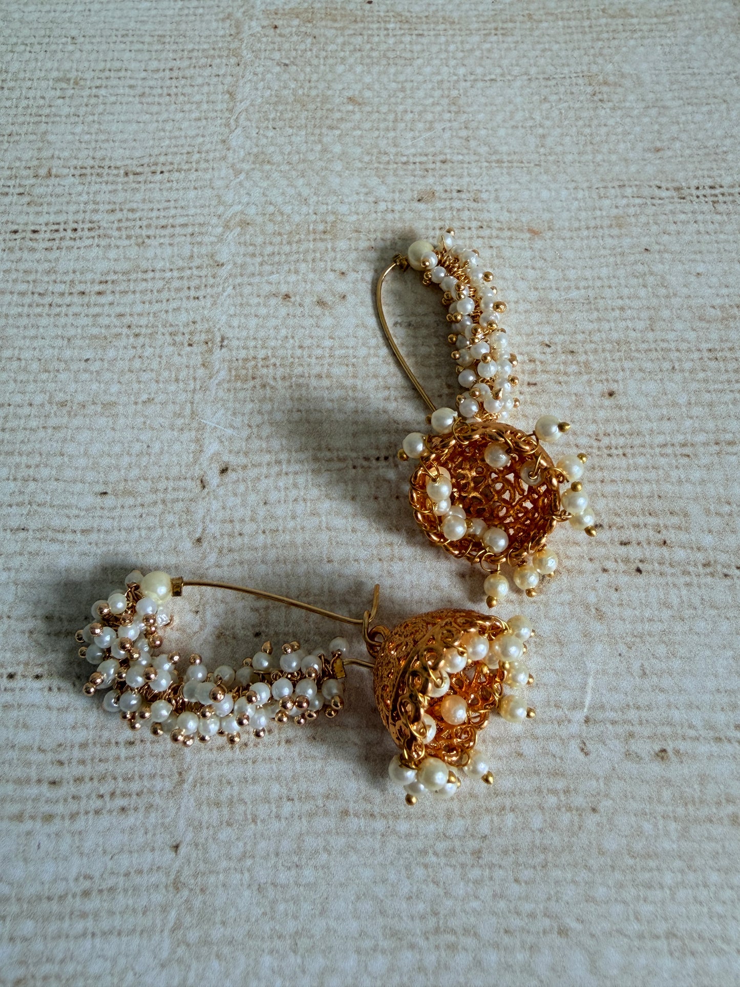 Pair of gold and pearl earrings on a textured beige fabric background