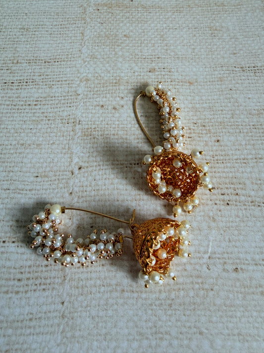 Pair of gold and pearl earrings on a textured beige fabric background